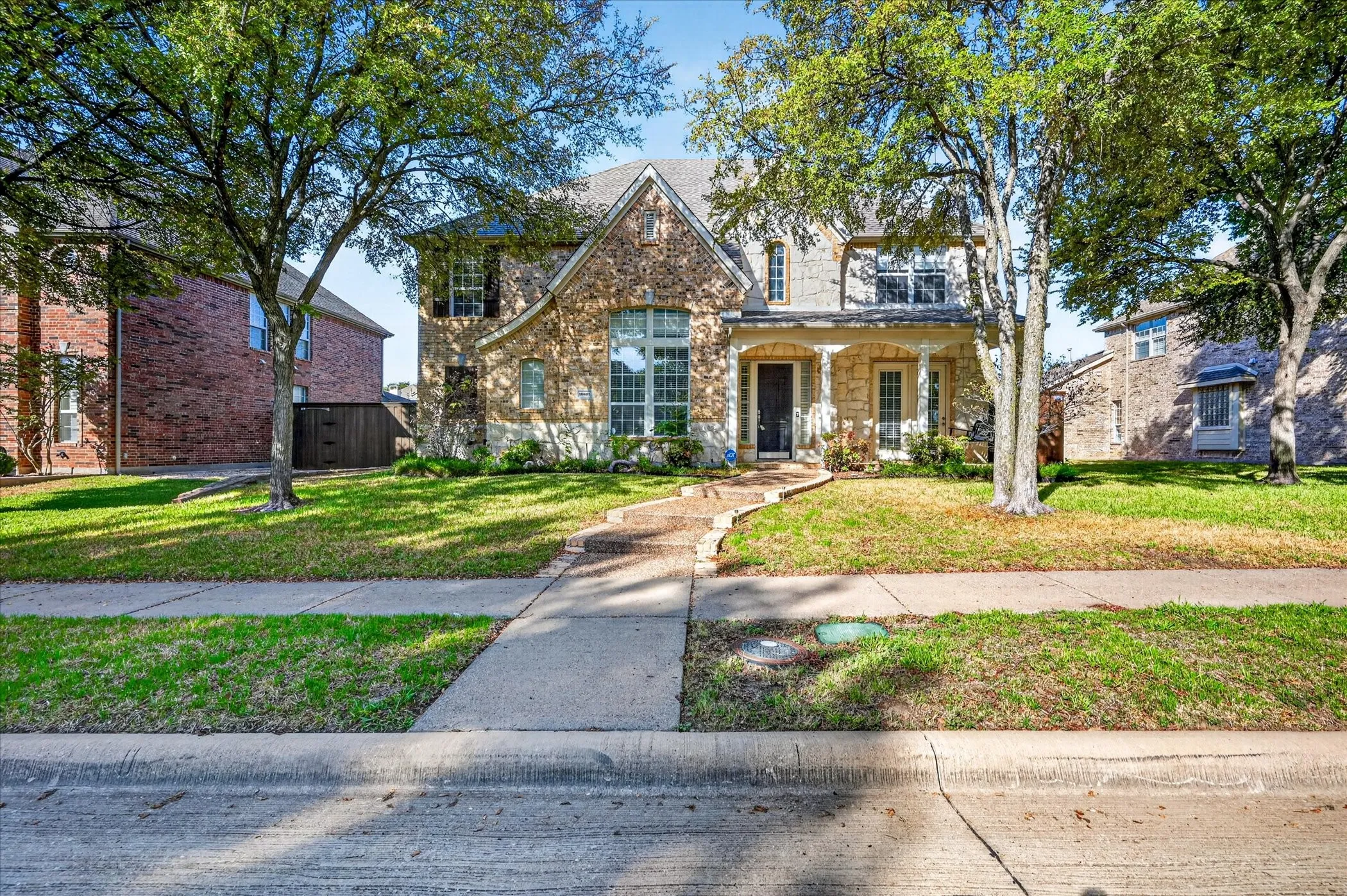 Charming two-story home featuring a mixed brick and stone exterior with arched entryway, complemented by mature landscaping and a manicured front lawn