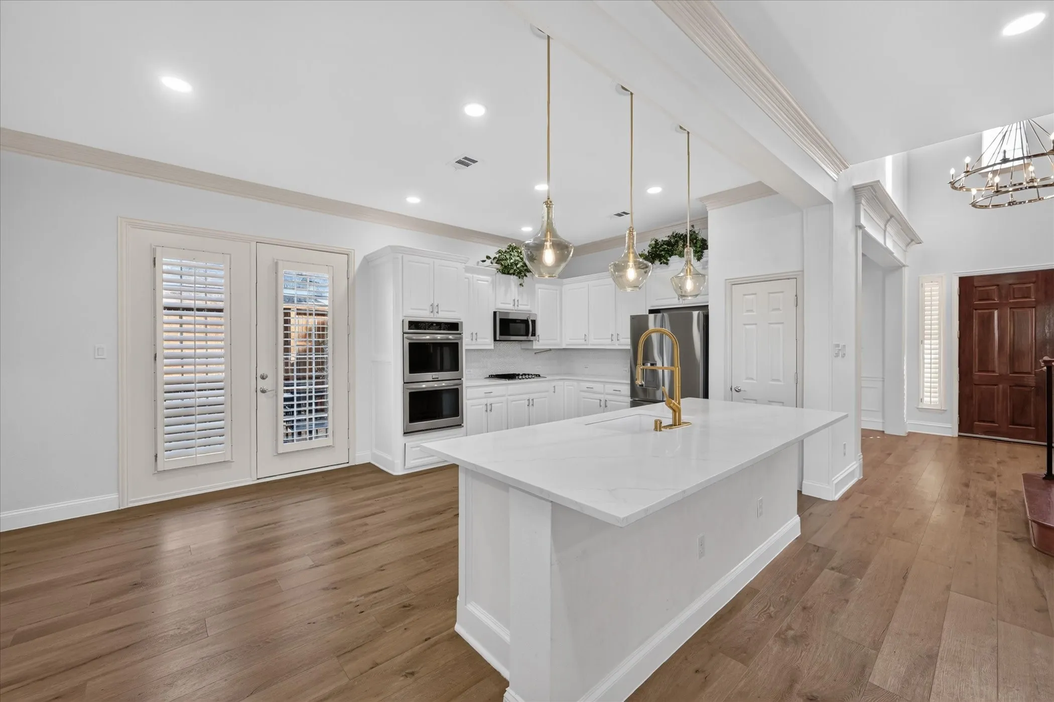 Kitchen featuring a large island with a gold-tone faucet, white cabinetry, built-in double ovens, and wood-finish flooring