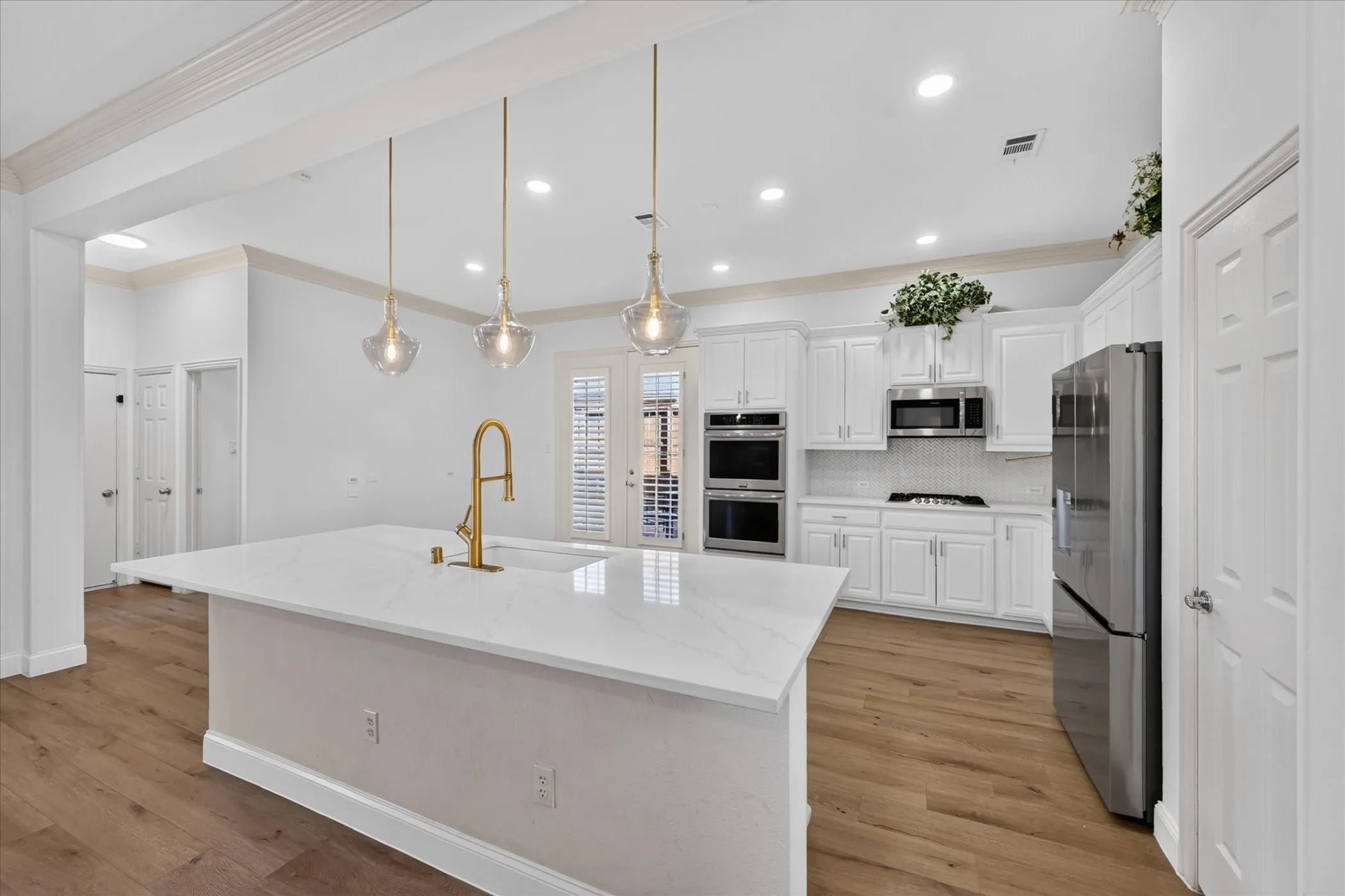 Kitchen featuring a large island with a surface-mount sink and gold-finish faucet, white cabinetry, integrated stainless steel appliances, and wood-finish flooring