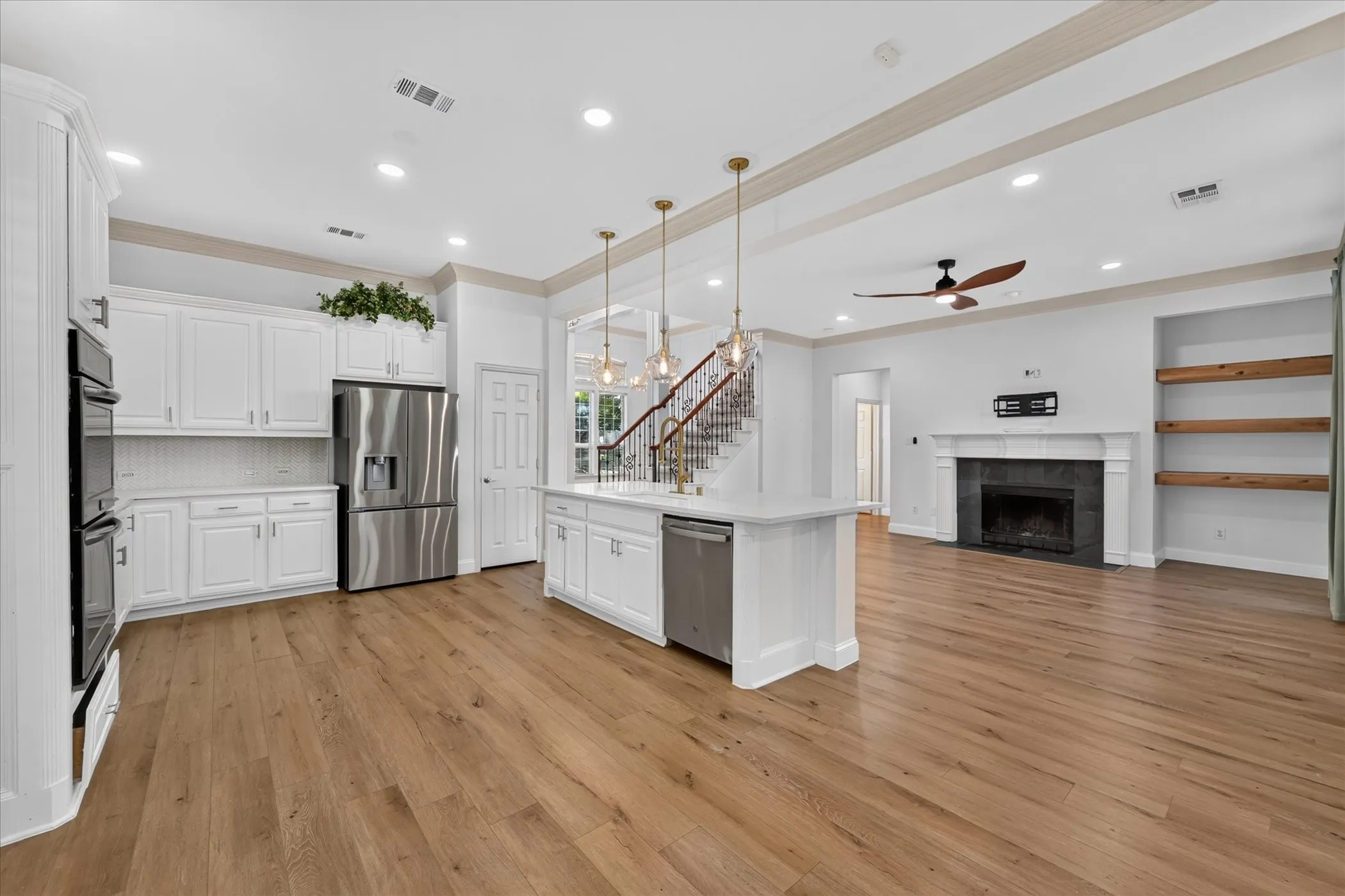 White shaker cabinetry, stainless steel appliances, wood-finish flooring, built-in fireplace, and integrated shelving
