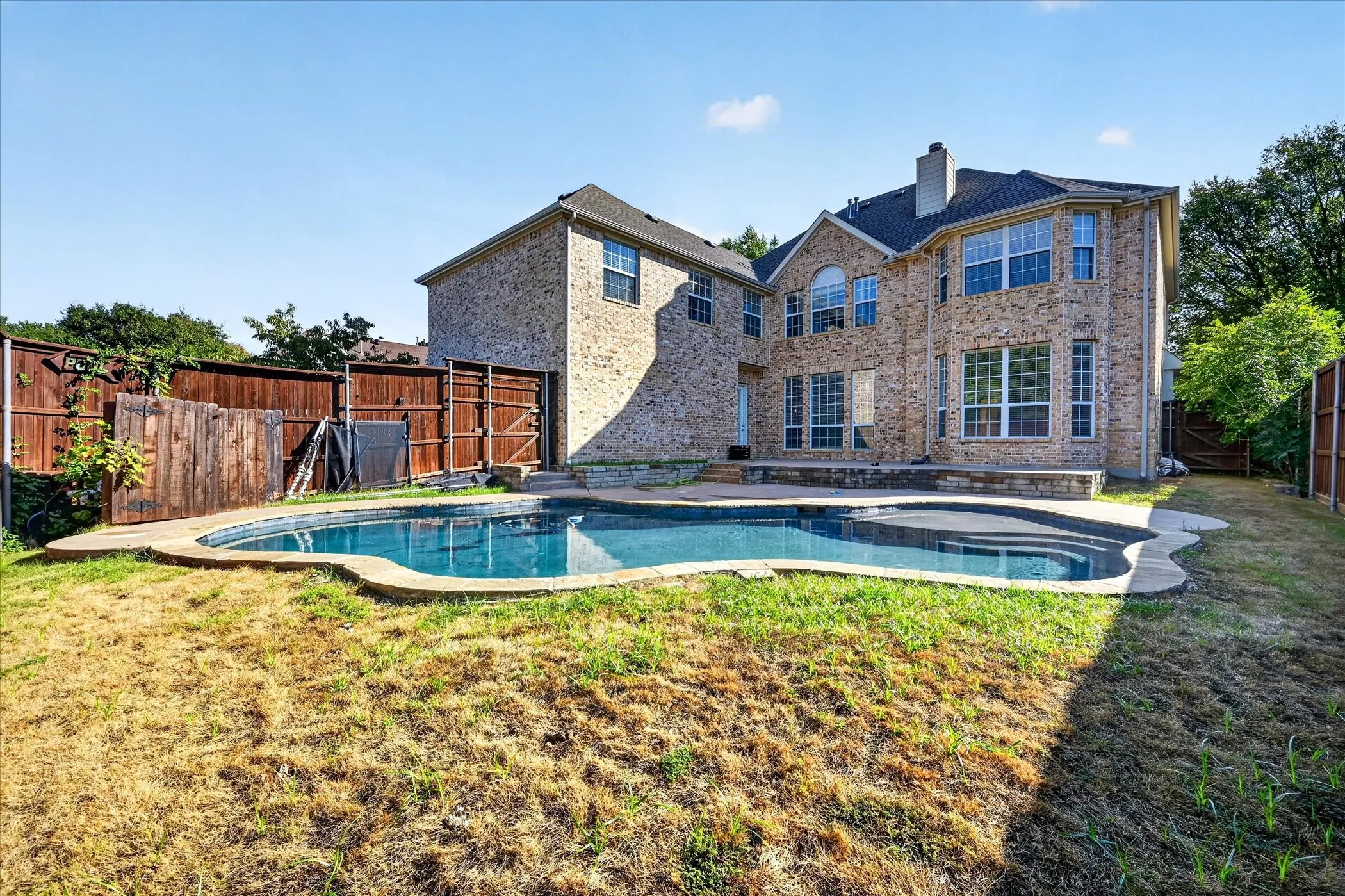Two-story brick exterior with multiple large windows, a structured in-ground swimming pool, and an integrated spa