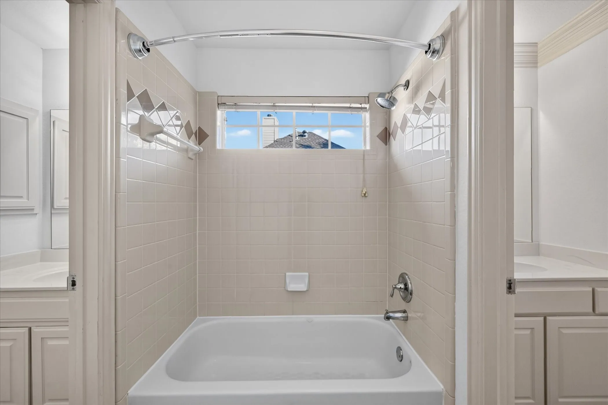Bathtub and shower combination with tiled surround, decorative accent tiling, a window, and chrome fixtures