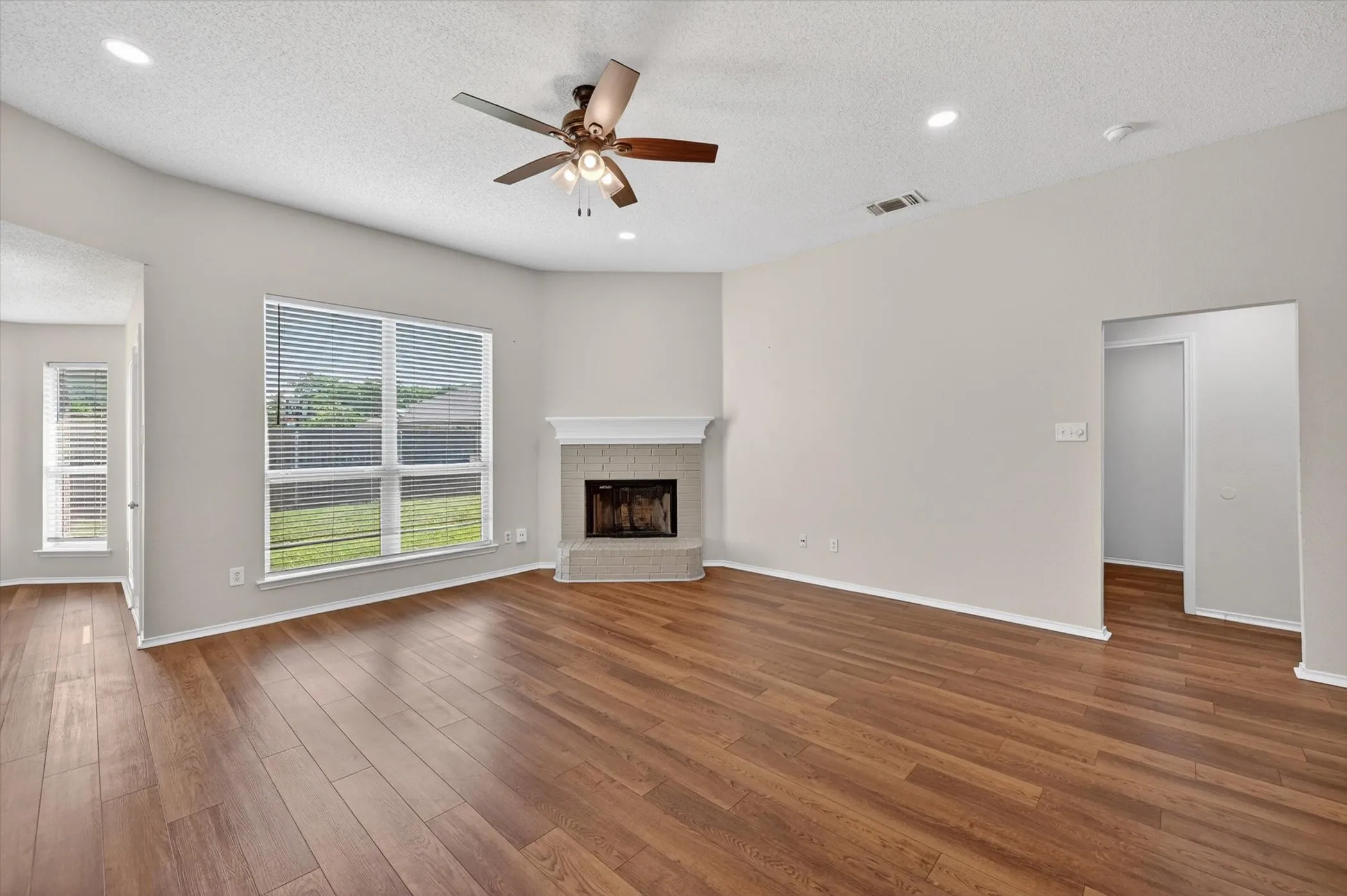 Wood-finish flooring, corner fireplace with hearth, multiple windows, recessed lighting, and a ceiling fan
