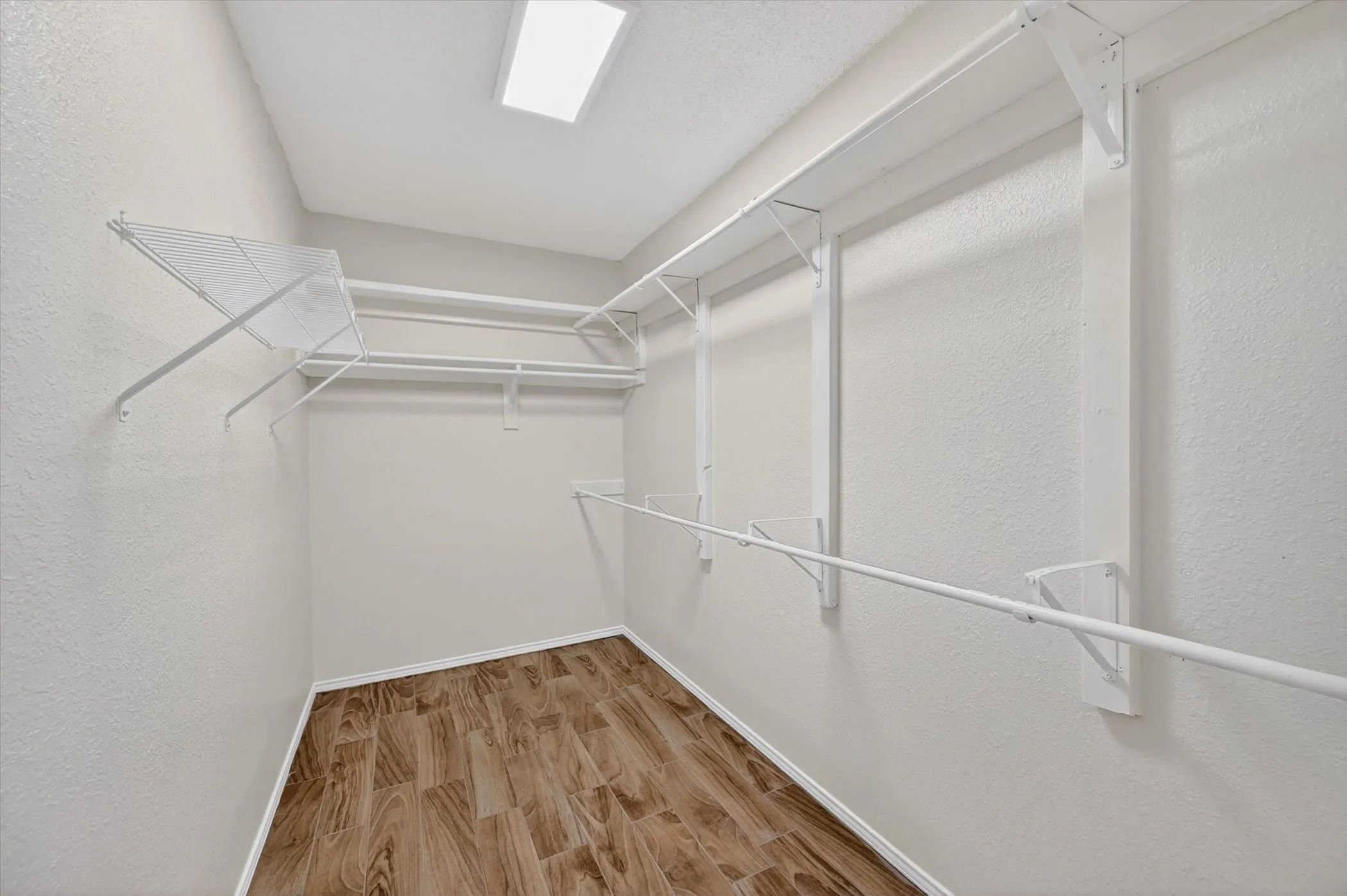 Spacious closet featuring wood-finish flooring, white wire shelving, and multiple hanging rods