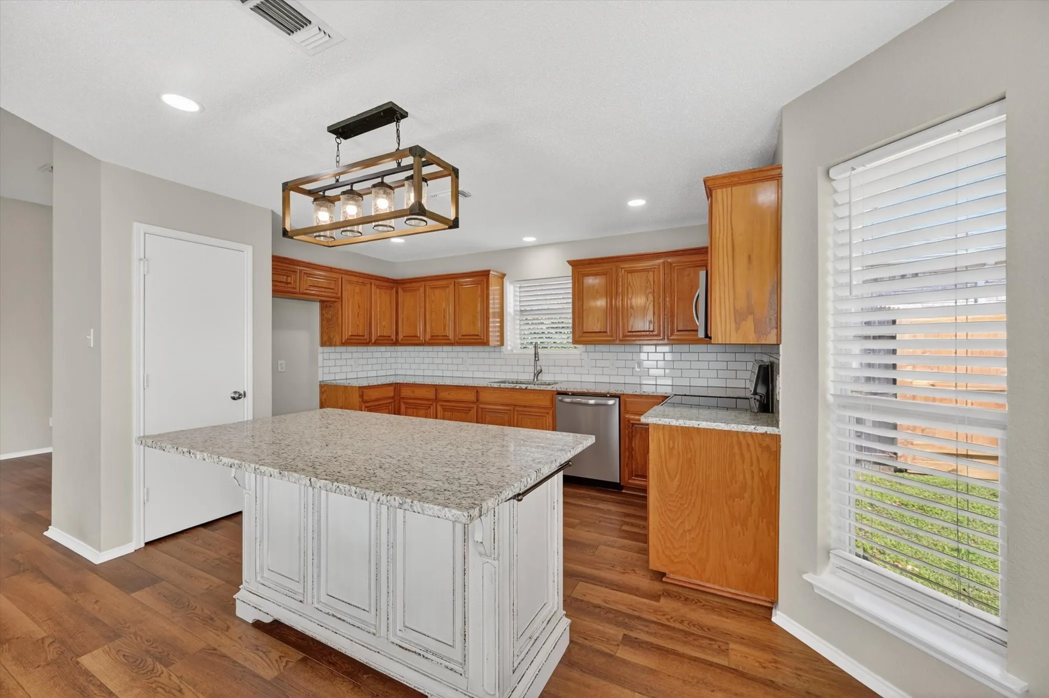 Kitchen featuring wood-finish flooring, a central island with a light-toned countertop, wood cabinetry, stainless steel appliances, and a subway tile backsplash