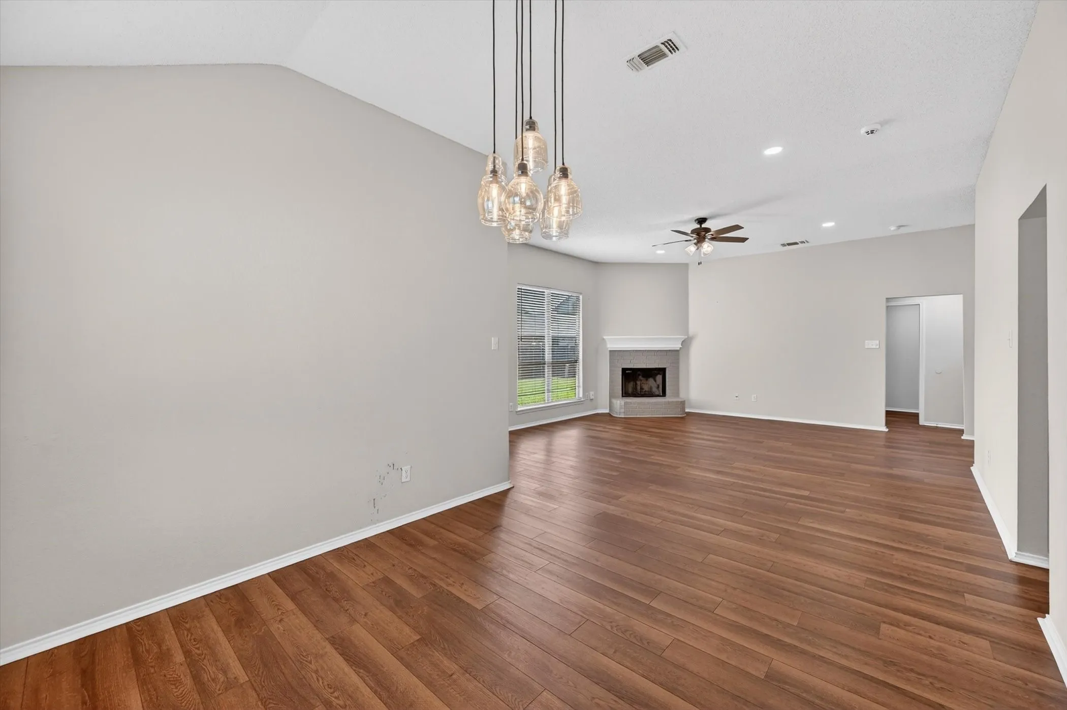 Wood-finish flooring, vaulted ceilings, and a corner fireplace with a white mantel