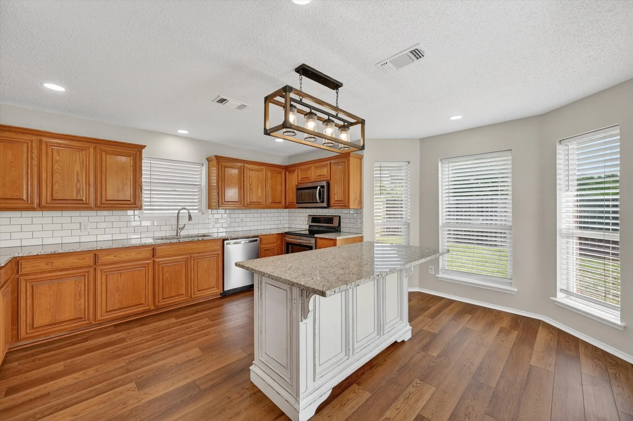 Kitchen featuring wood-finish flooring, wood cabinetry, stainless steel appliances, a center island with a light-colored countertop, and a tiled backsplash