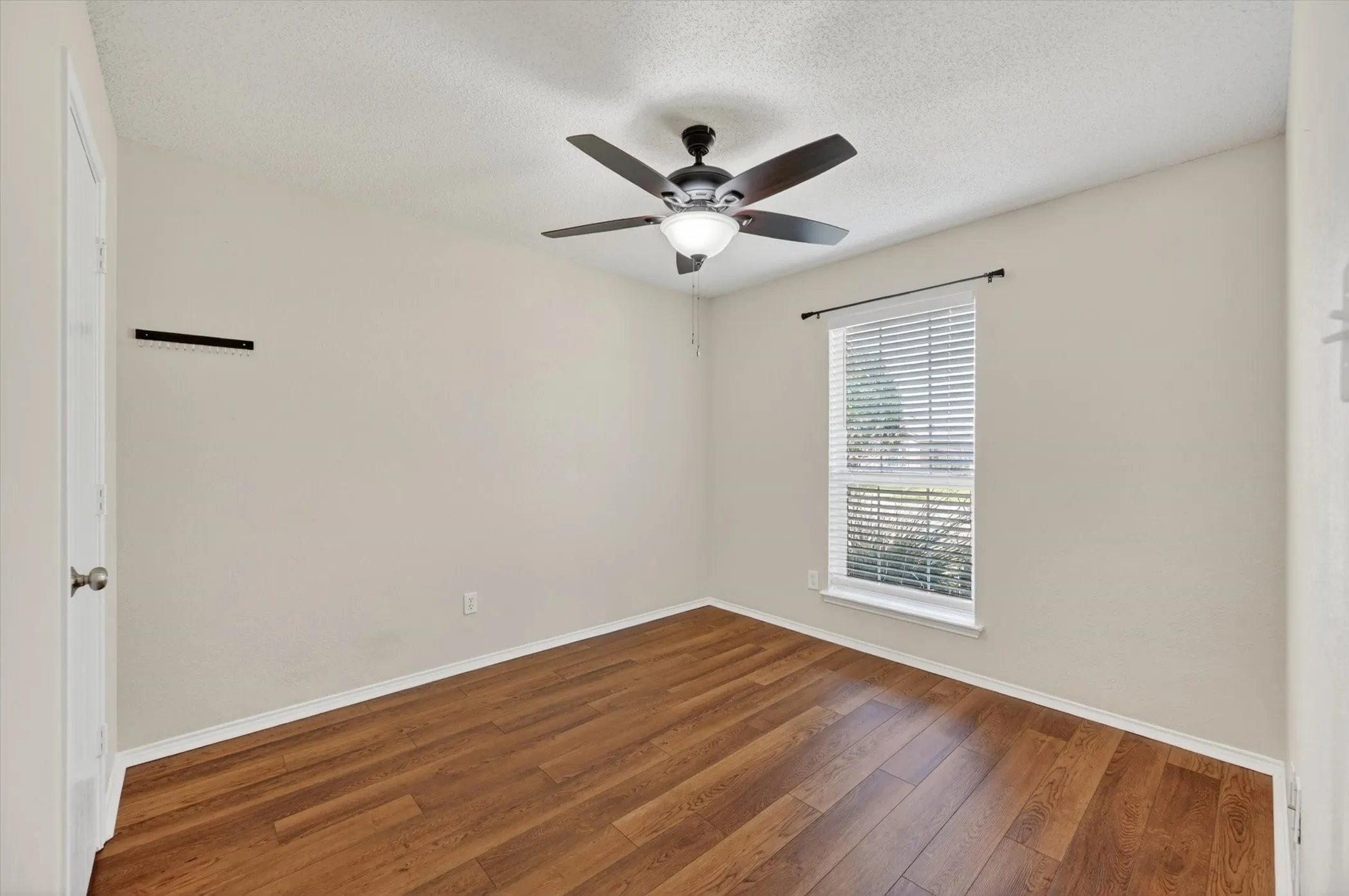 Wood-finish flooring, single window with blinds, ceiling fan with integrated lighting, and neutral wall tones