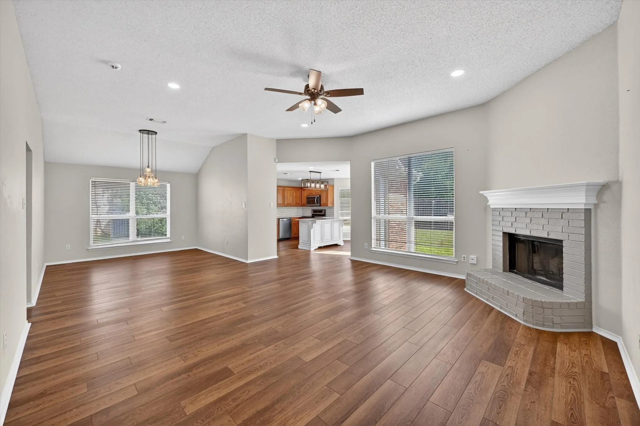 Vaulted ceilings, wood-finish flooring, recessed lighting, and a fireplace with a painted brick surround