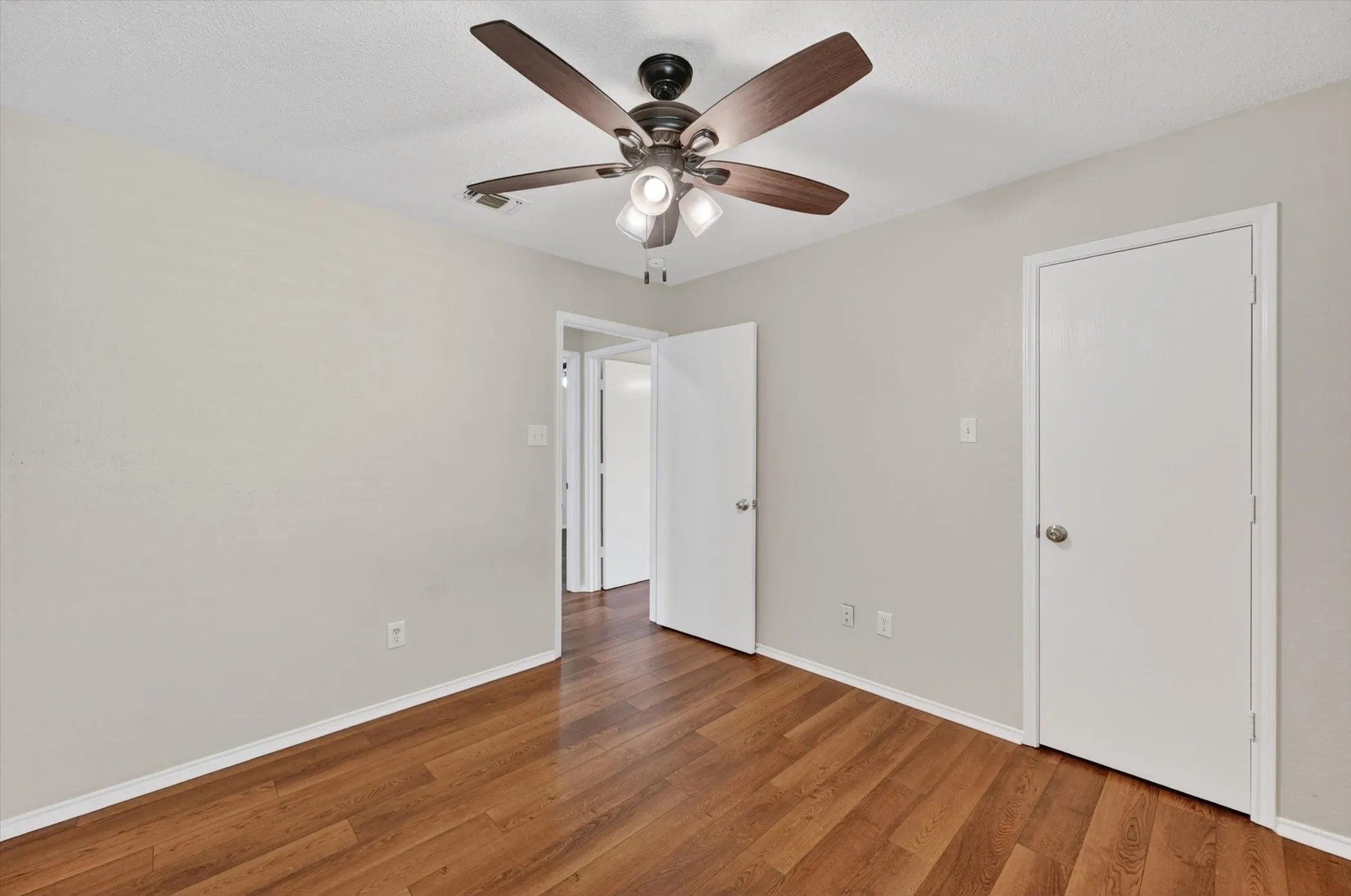 Wood-finish flooring, light neutral wall paint, and a ceiling fan with integrated lighting