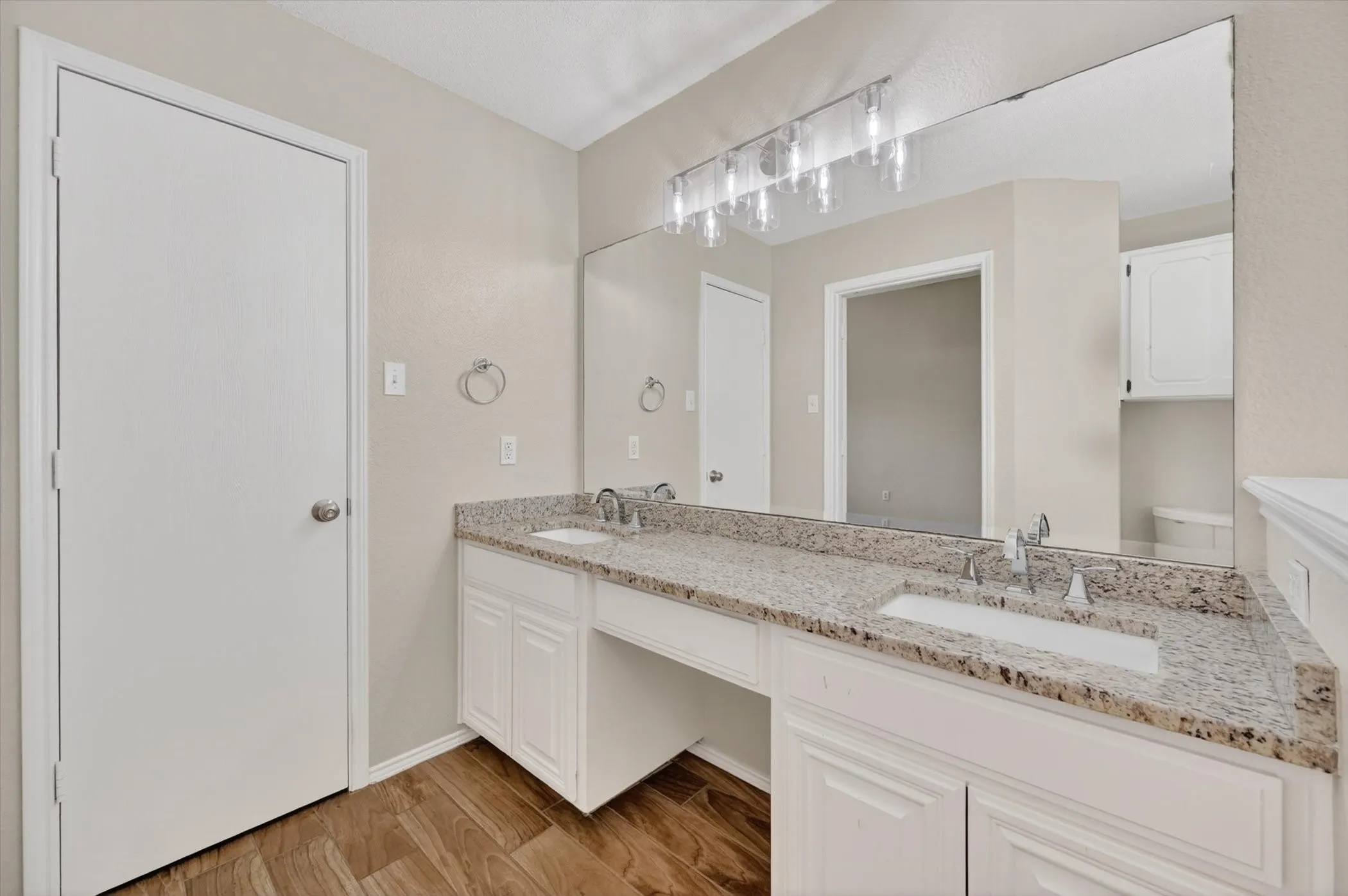 Double vanity with granite countertop, integrated sinks, white cabinetry, and wood-finish flooring