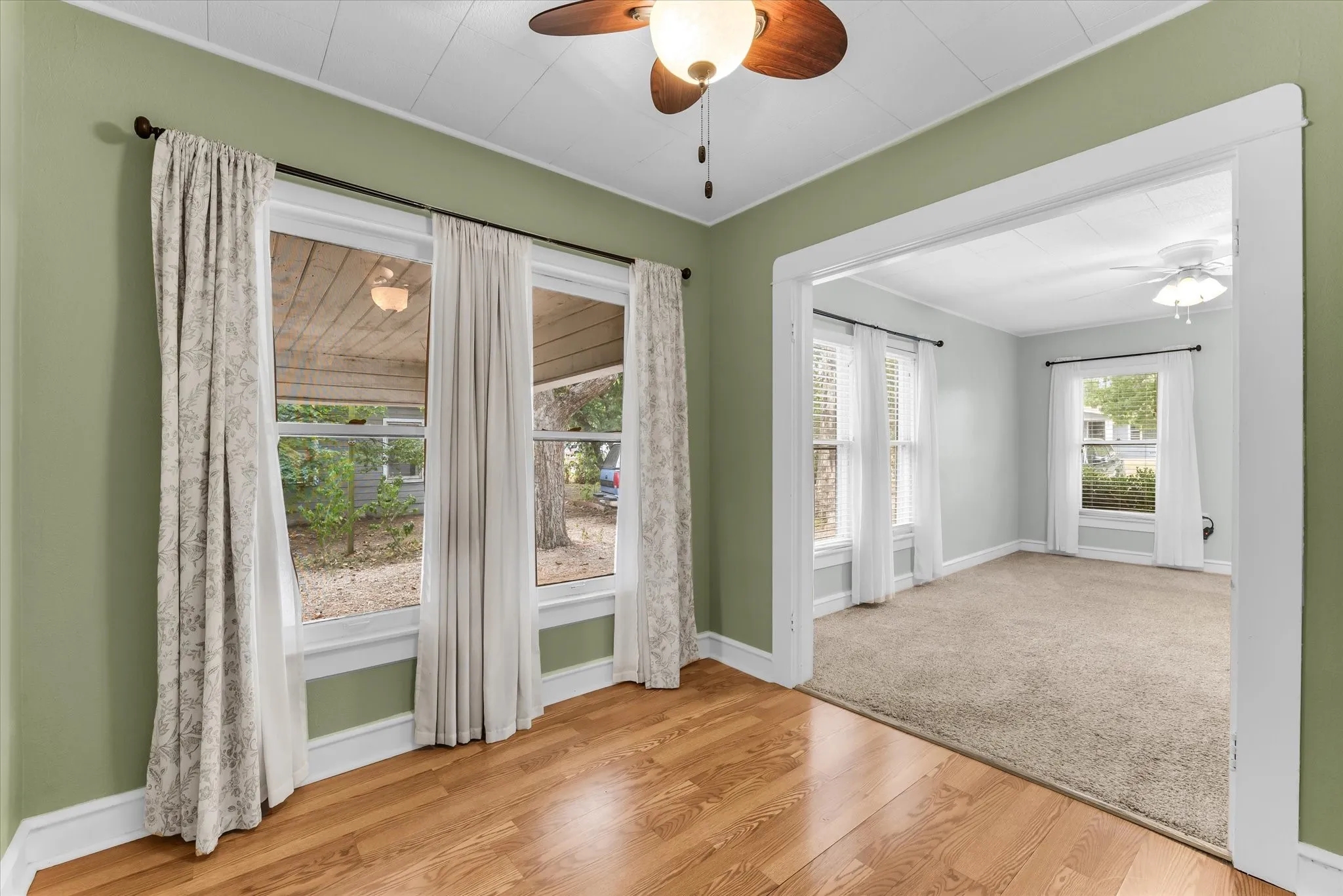Warm wood-finish flooring, light green wall paint, and a ceiling fan with integrated lighting