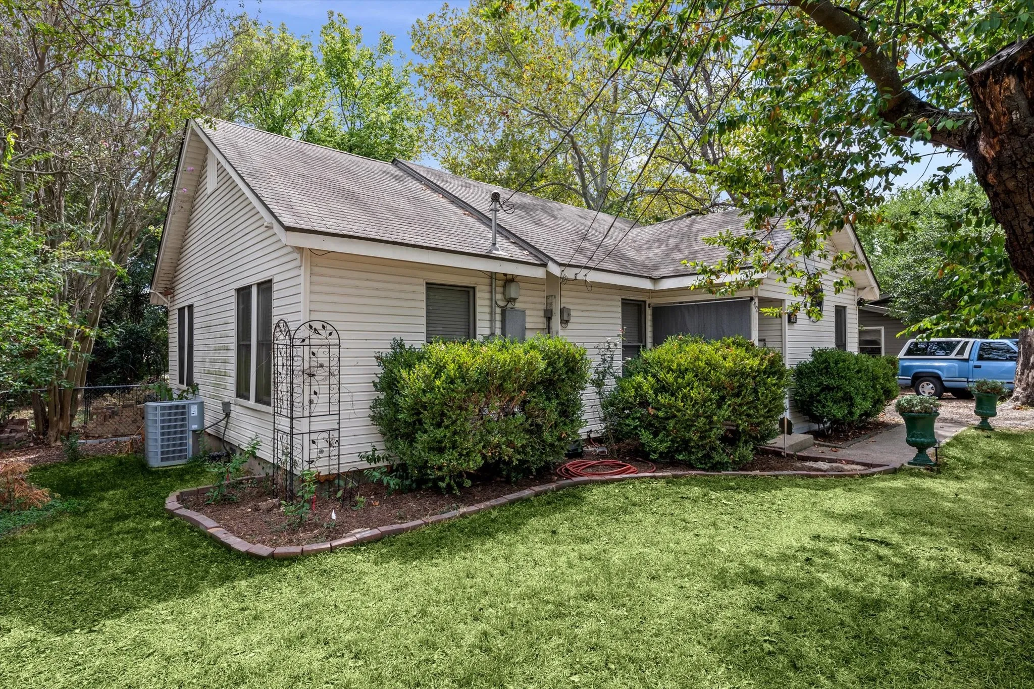 Exterior featuring white siding, a sloped roof, and established landscaping with manicured shrubs