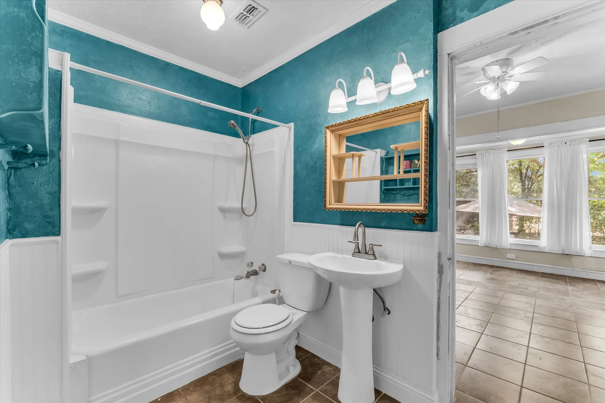Tub and shower combination with a pedestal sink, framed mirror, and tile flooring