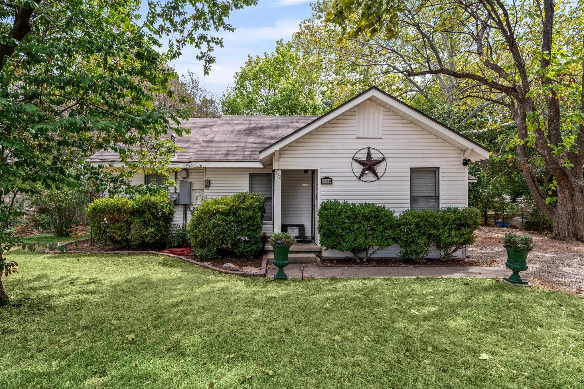 White siding exterior, gabled roofline, mature trees, landscaped shrubbery, and a manicured lawn