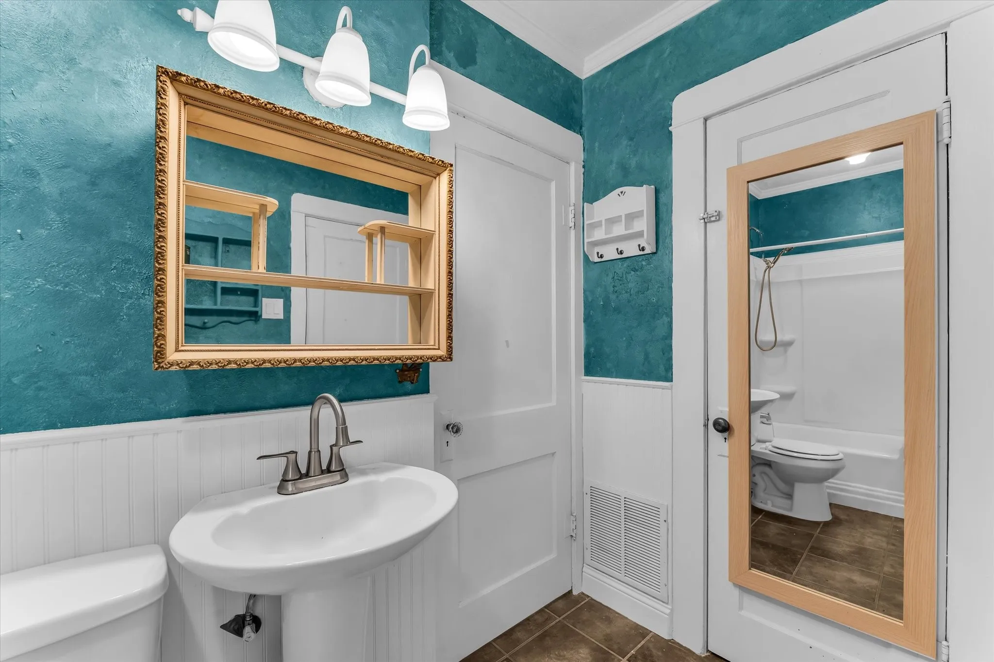 Pedestal sink with brushed nickel faucet, decorative framed mirror, textured wall finish, white wainscoting, and tile flooring