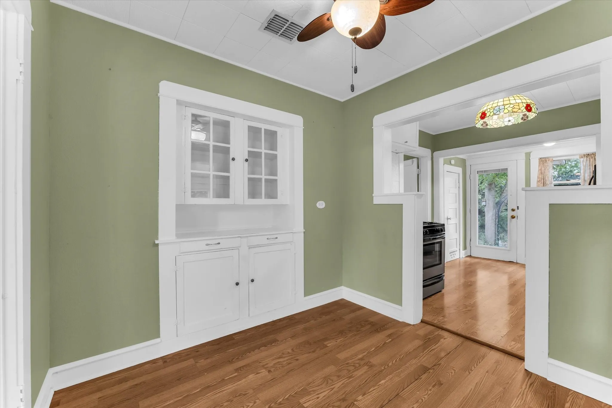 Built-in cabinetry with glass-front uppers, wood-finish flooring, ceiling fan, and decorative light fixture
