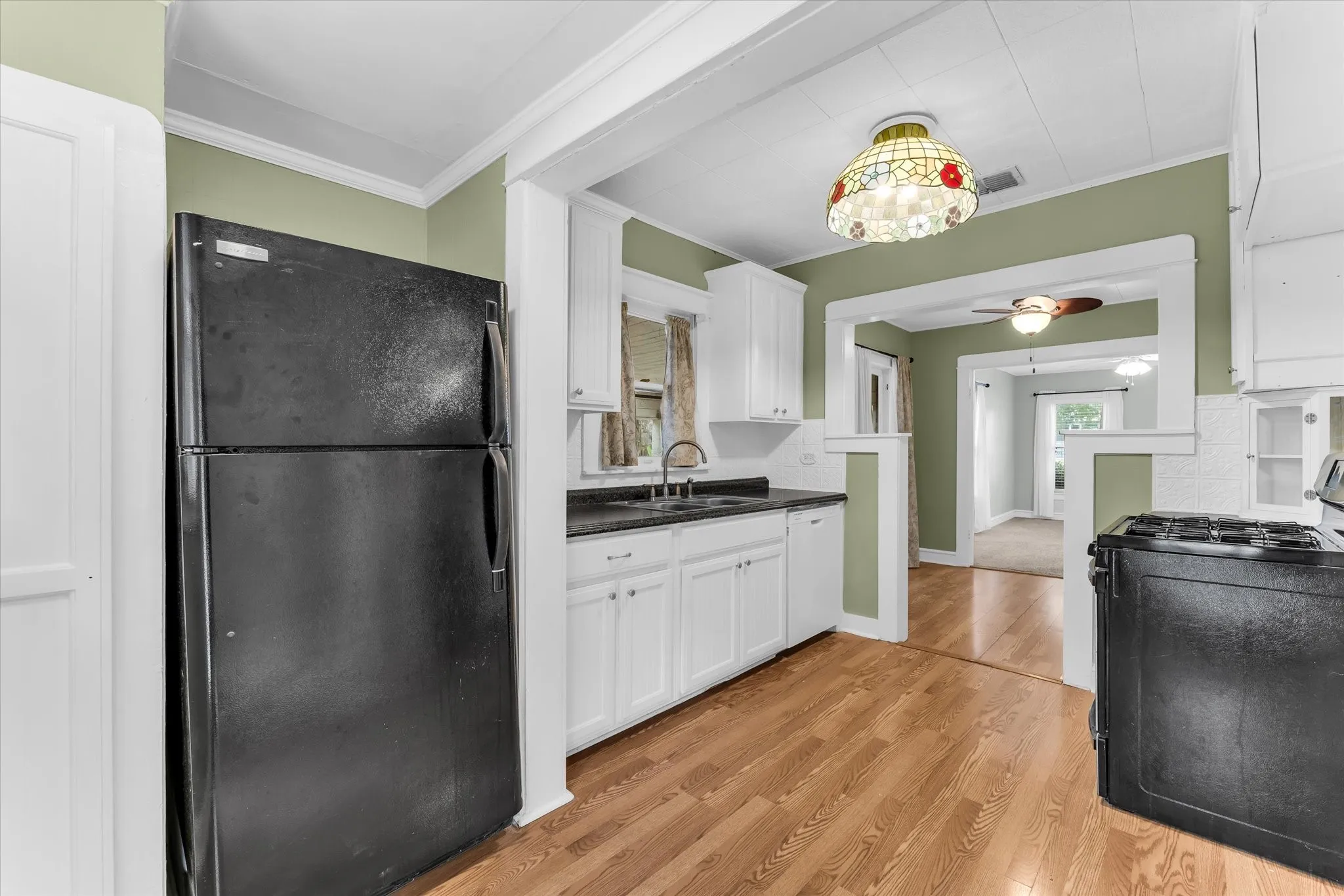 Kitchen featuring wood-finish flooring, white cabinetry, a black refrigerator, a black range, and a decorative ceiling light fixture