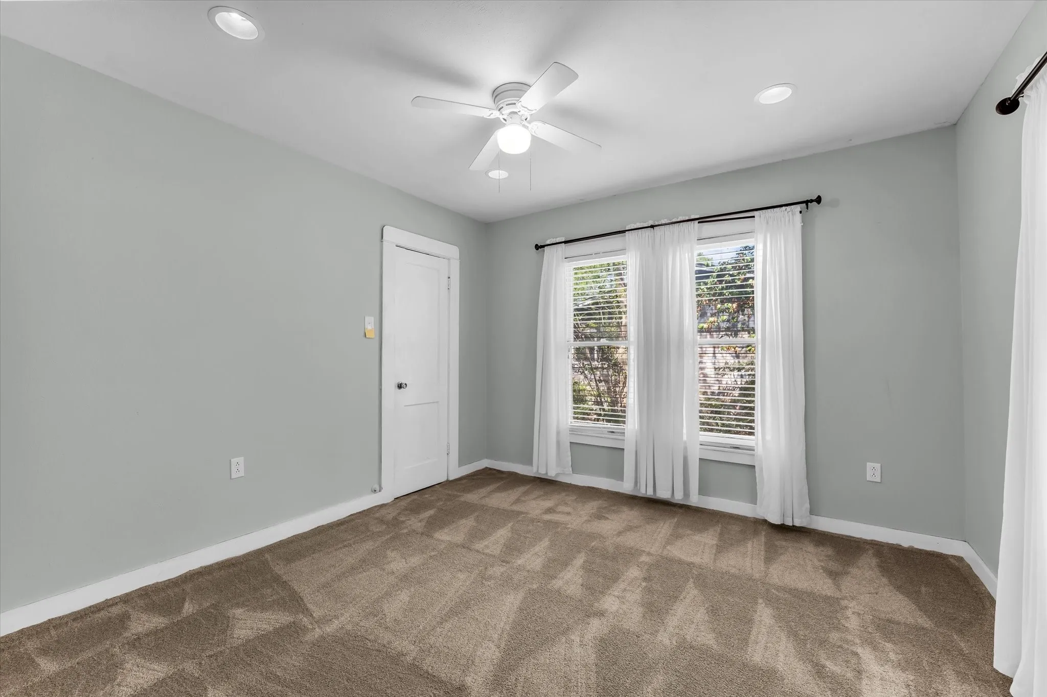 Recessed ceiling lighting, ceiling fan, neutral wall color, two windows with blinds, and brown patterned carpet