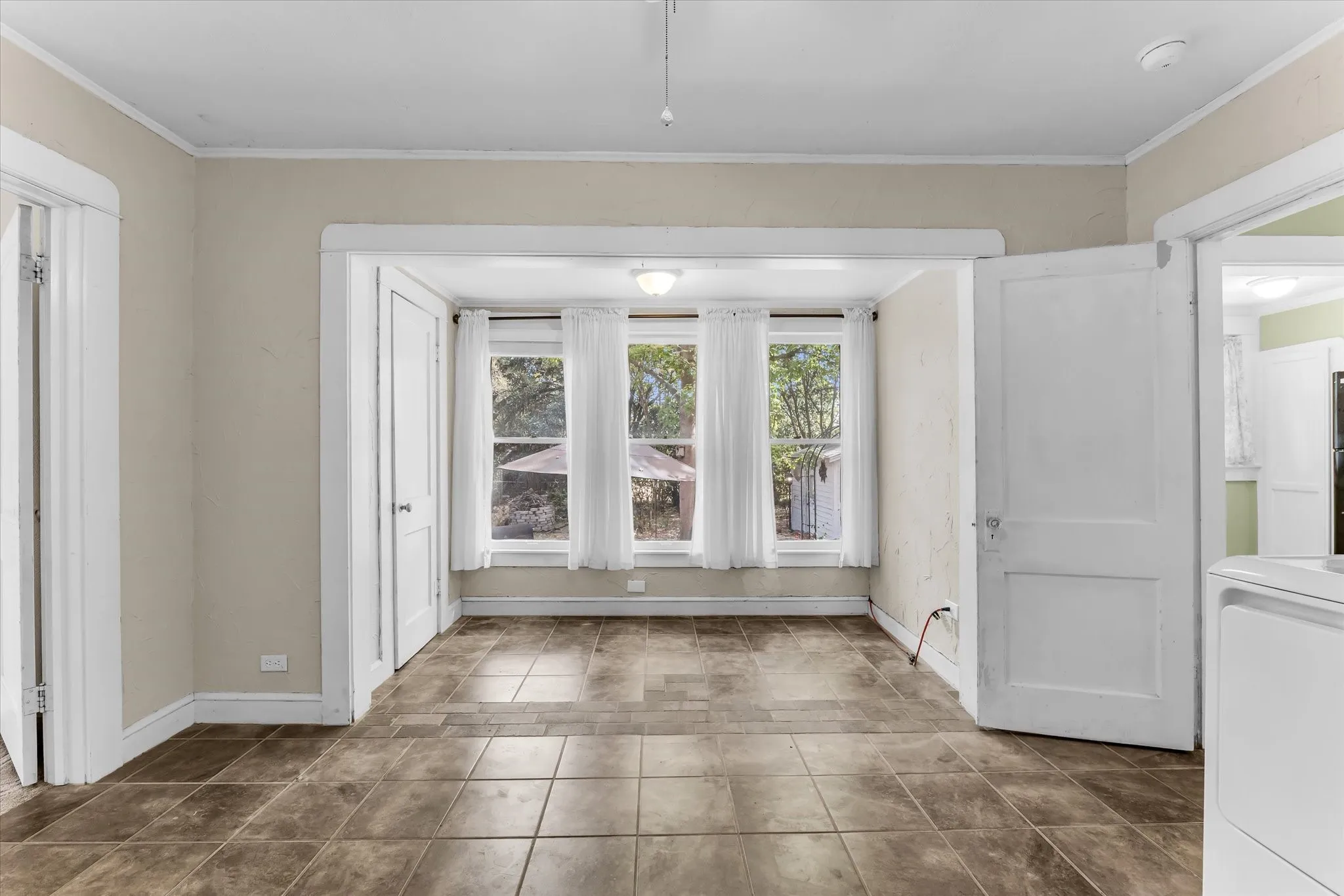Brown tile flooring, white trim, and three windows with white curtains