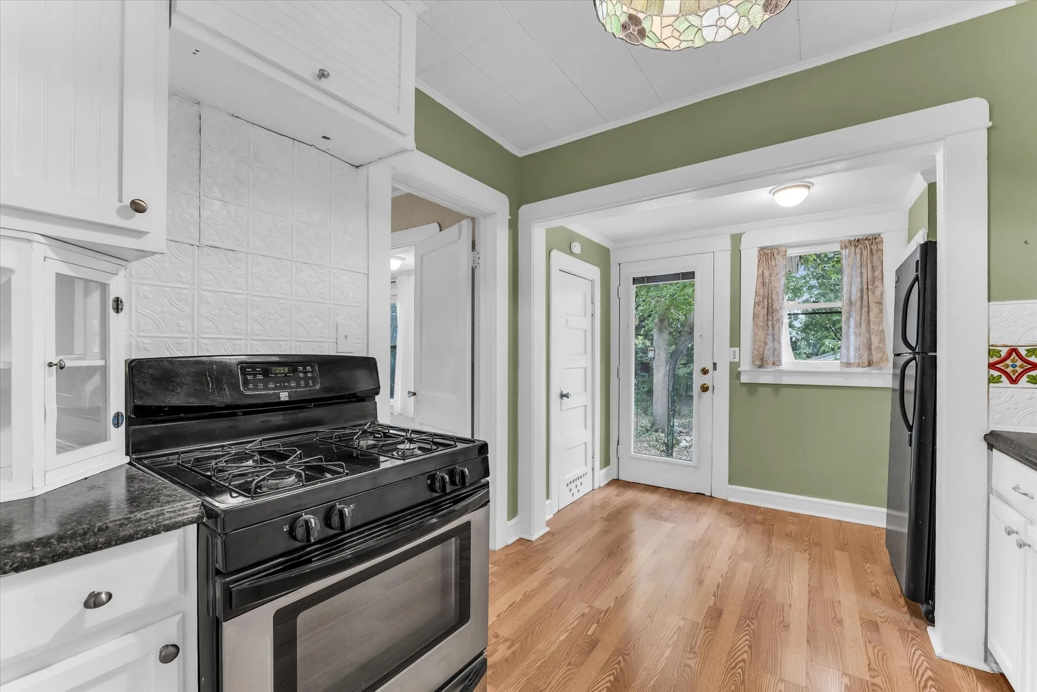 Kitchen featuring white cabinetry, a built-in oven range, black stone-finish countertops, wood-finish flooring, and a glass-paneled door
