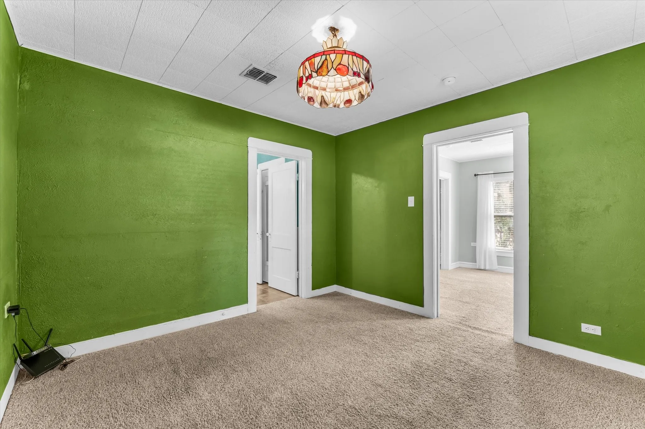 Textured green wall finish, white ceiling with paneling, stained glass chandelier, and neutral carpet flooring