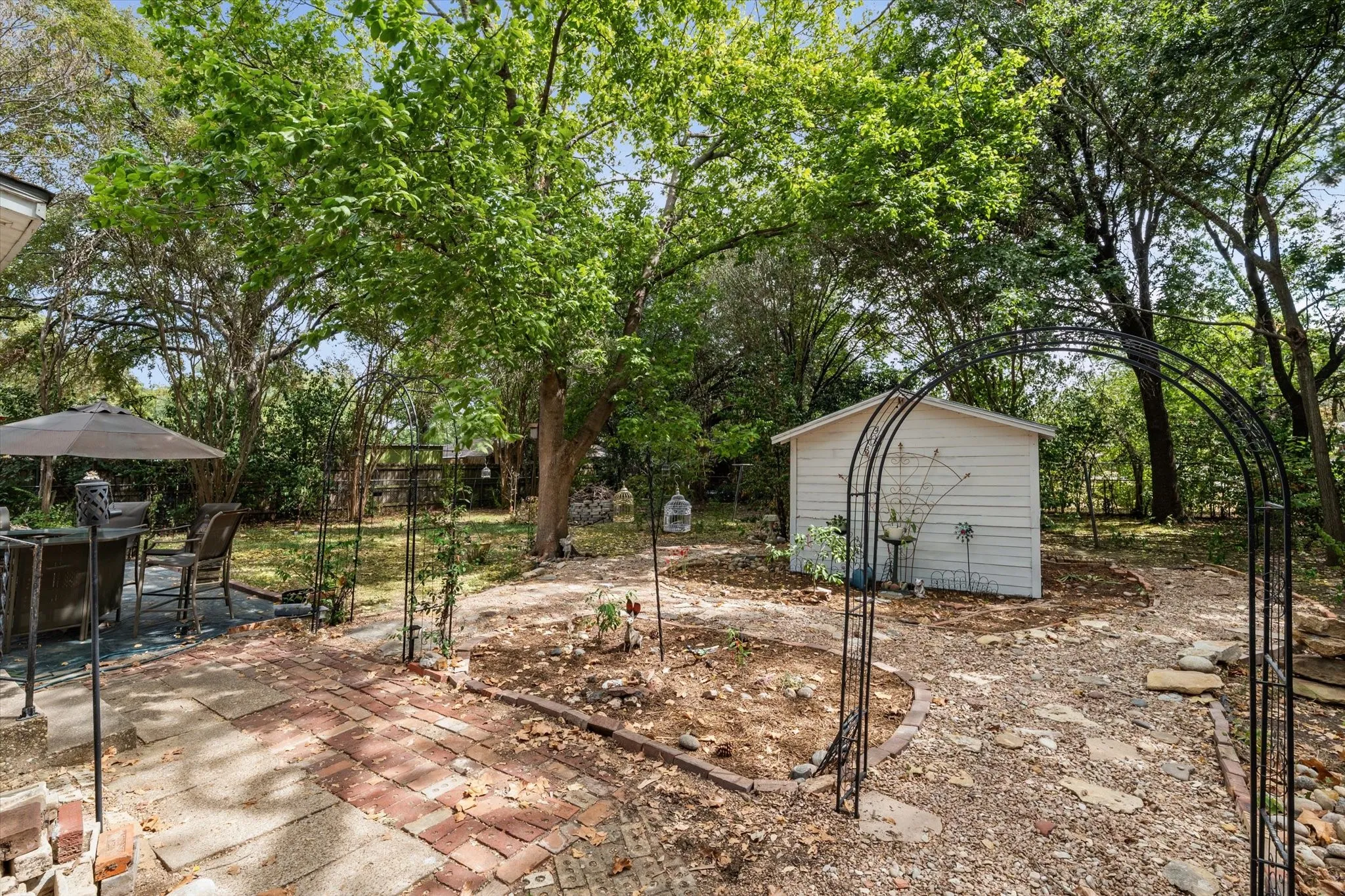 Expansive outdoor space featuring a brick patio, mature trees, a storage shed, and decorative metal archways