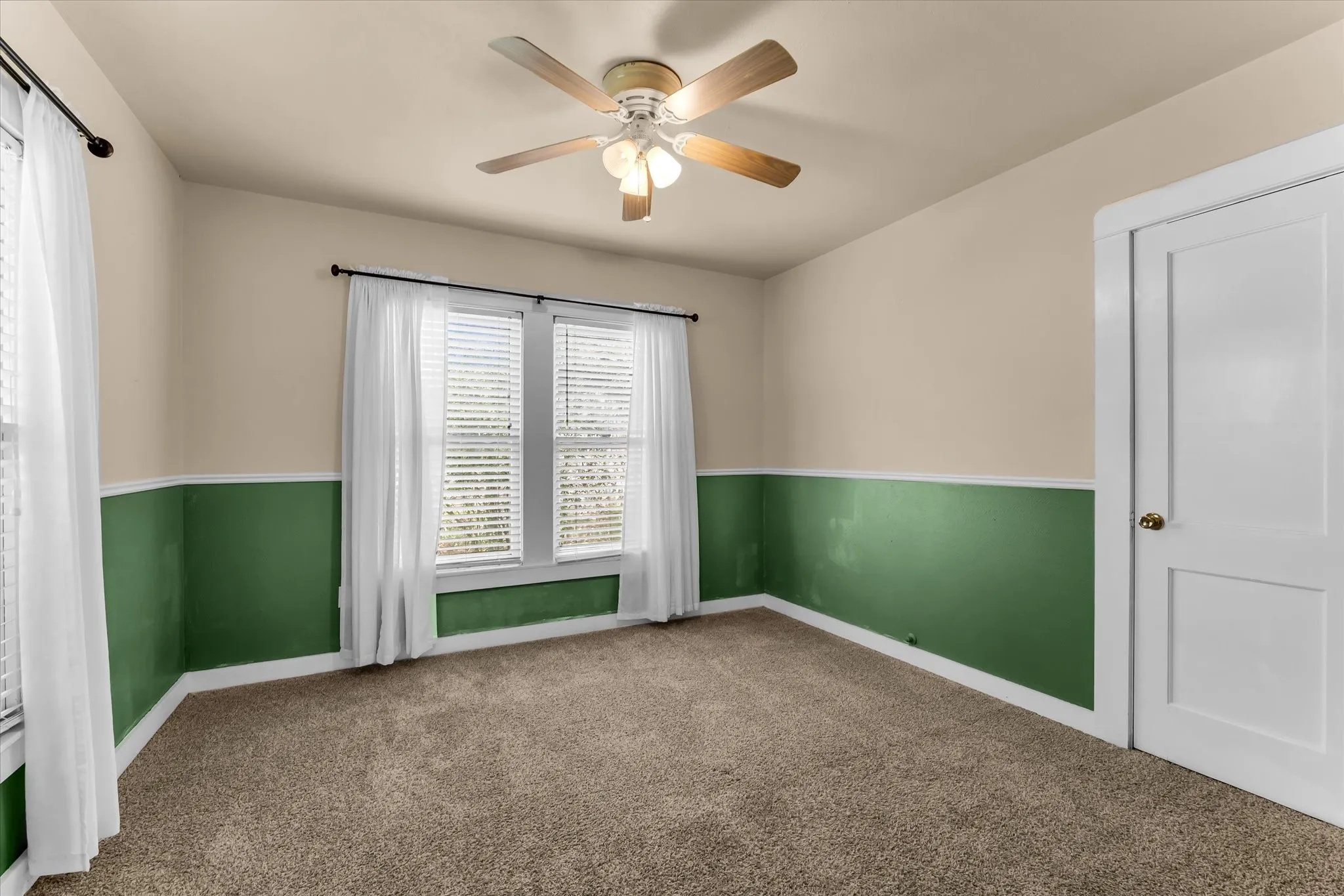 Carpeted room featuring a ceiling fan with light fixture, dual windows with blinds, and two-tone wall treatment