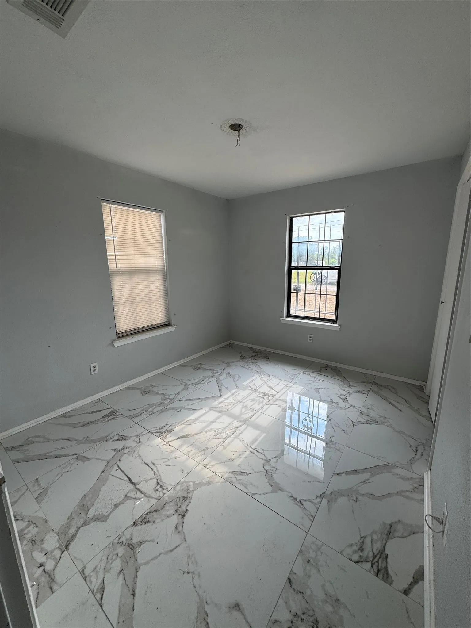 Spacious room featuring large format tile flooring, two windows, and neutral wall tones