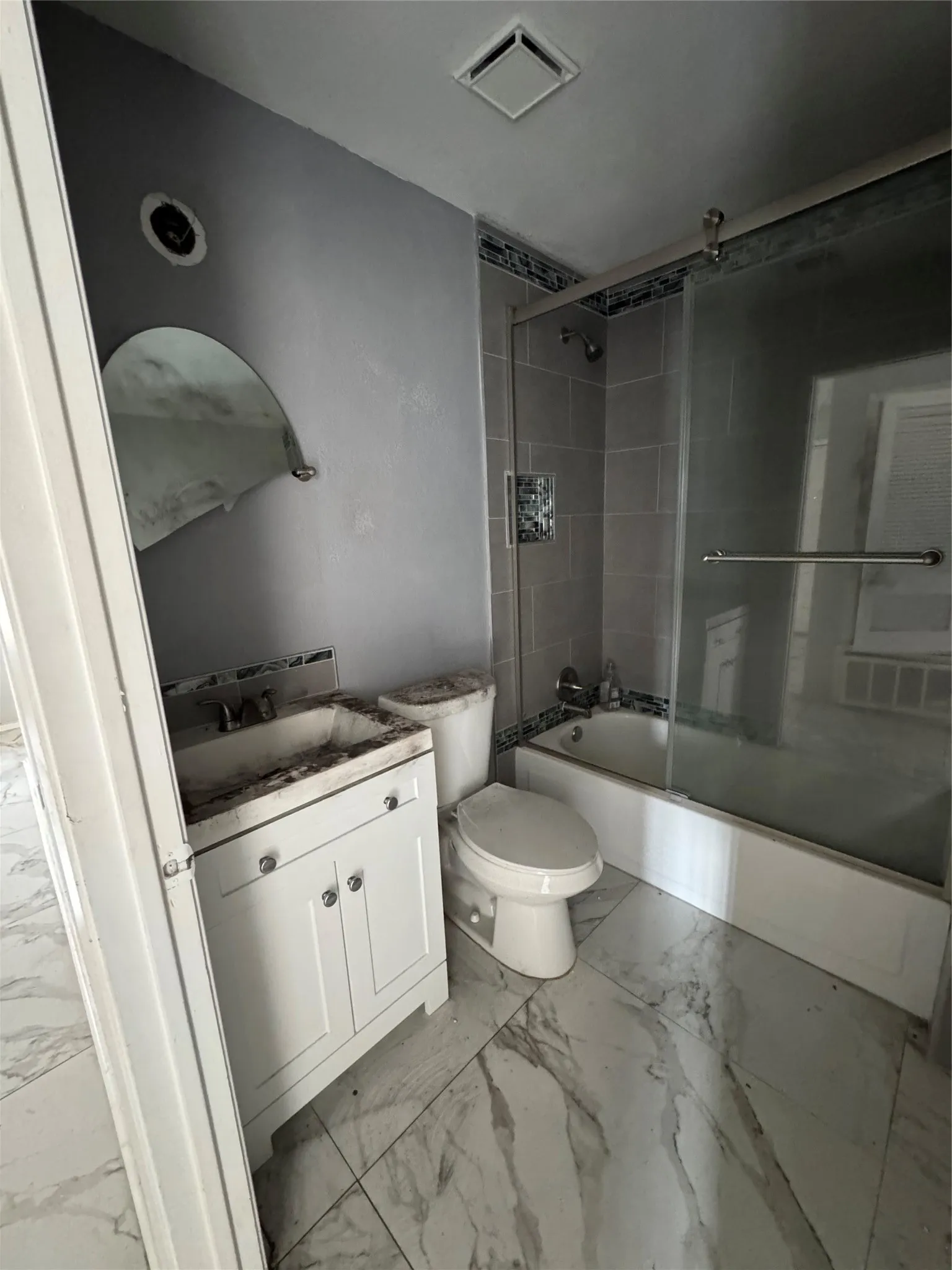 White vanity with base cabinetry, wall-mounted mirror, white toilet, and a tiled shower with a sliding glass enclosure