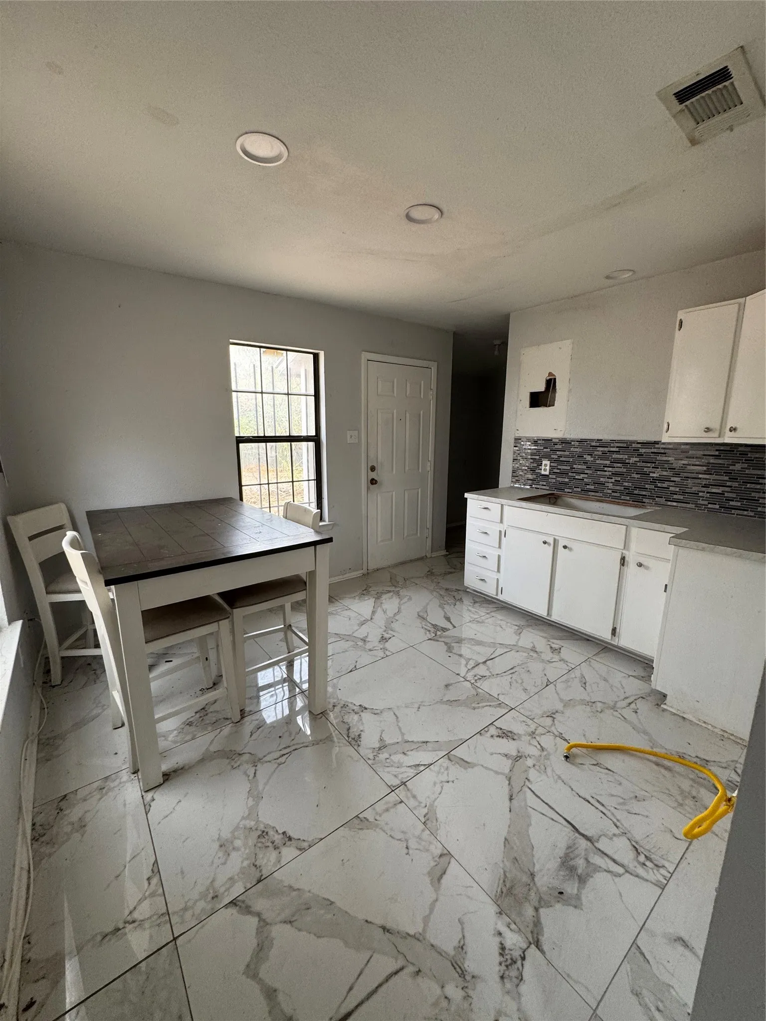 Recessed ceiling lighting, large format tile flooring, white cabinetry, dark countertop, and mosaic tile backsplash