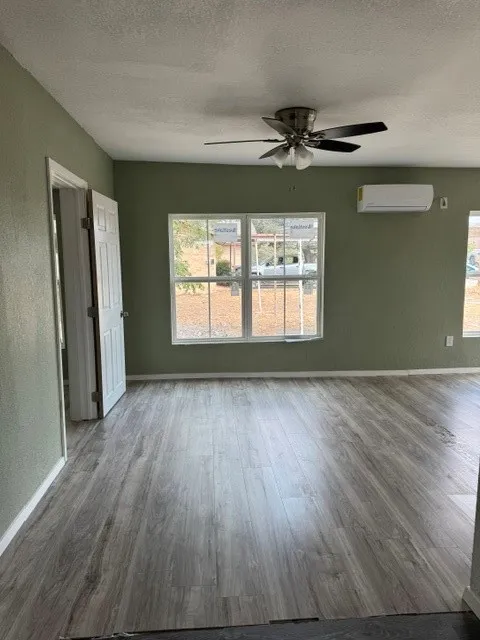 Wood-finish flooring, light green walls, ceiling fan with integrated lighting, multiple windows, and a wall-mounted climate control unit