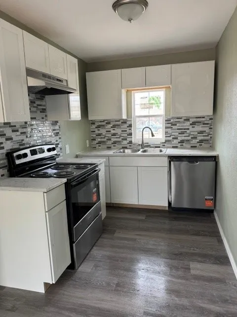 Kitchen featuring white cabinetry, a mosaic tile backsplash, wood-finish flooring, and stainless steel appliances