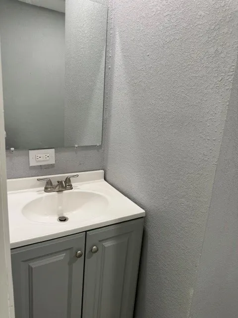 Vanity with a white countertop and integrated sink, brushed nickel faucet, and gray cabinetry with knob hardware