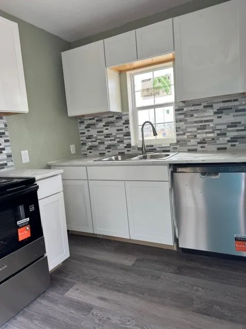 White cabinetry, stone-look countertops, stainless steel appliances, multi-tone tile backsplash, and wood-finish flooring