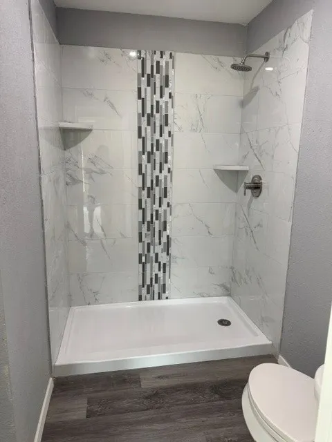 Walk-in shower featuring marble-look tile, decorative mosaic tile accent, and dual built-in corner shelves
