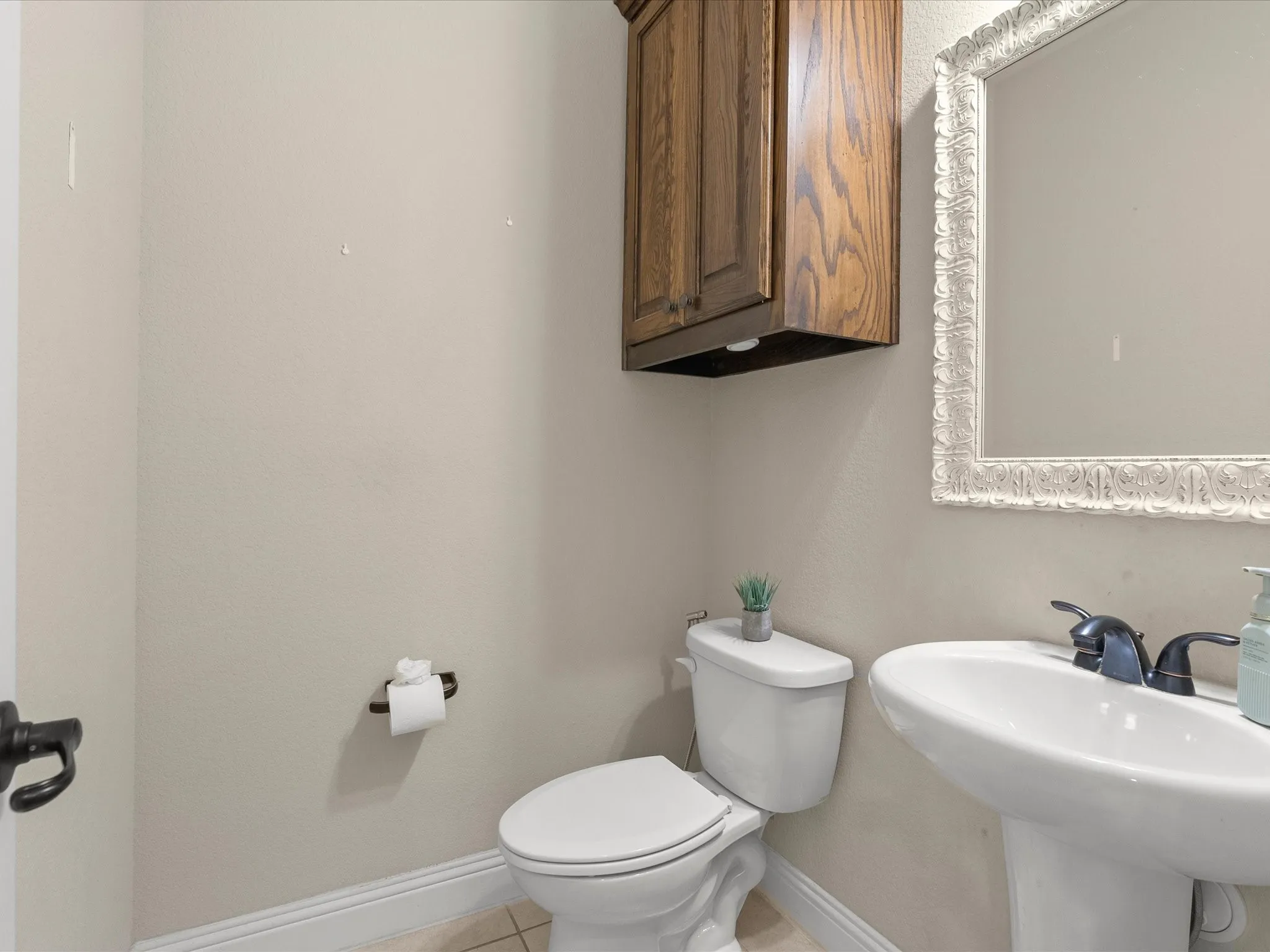 Pedestal sink with dark bronze faucet, white toilet, and an ornate framed mirror