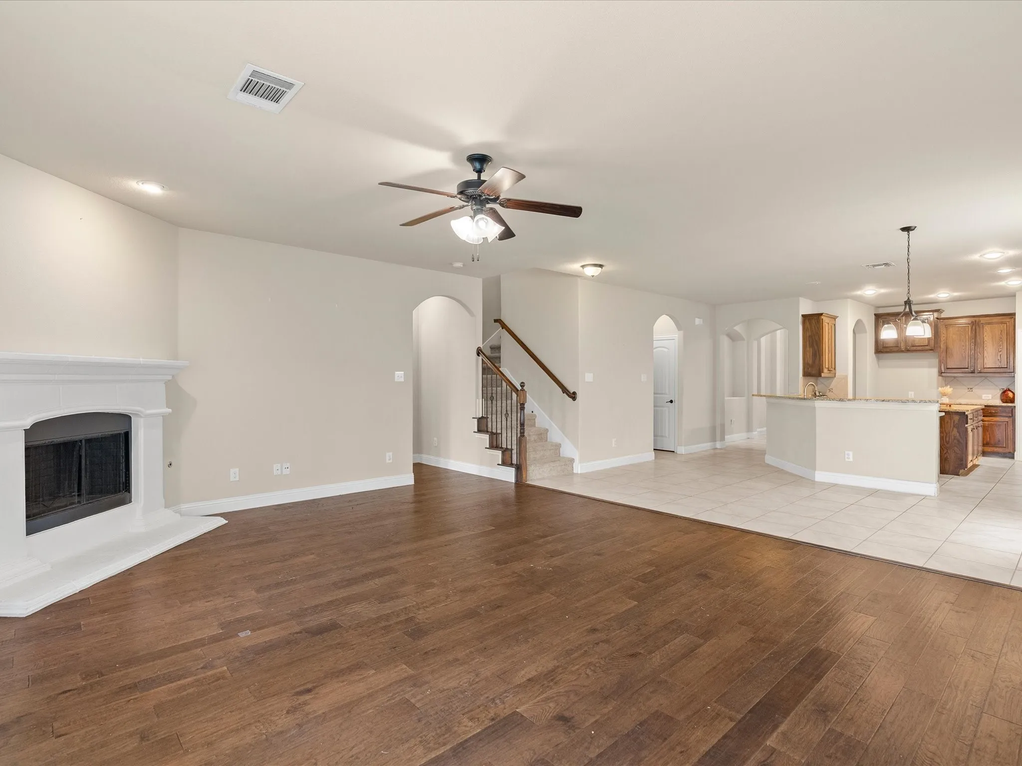 Spacious main living area featuring wood-finish flooring and a white mantel fireplace
