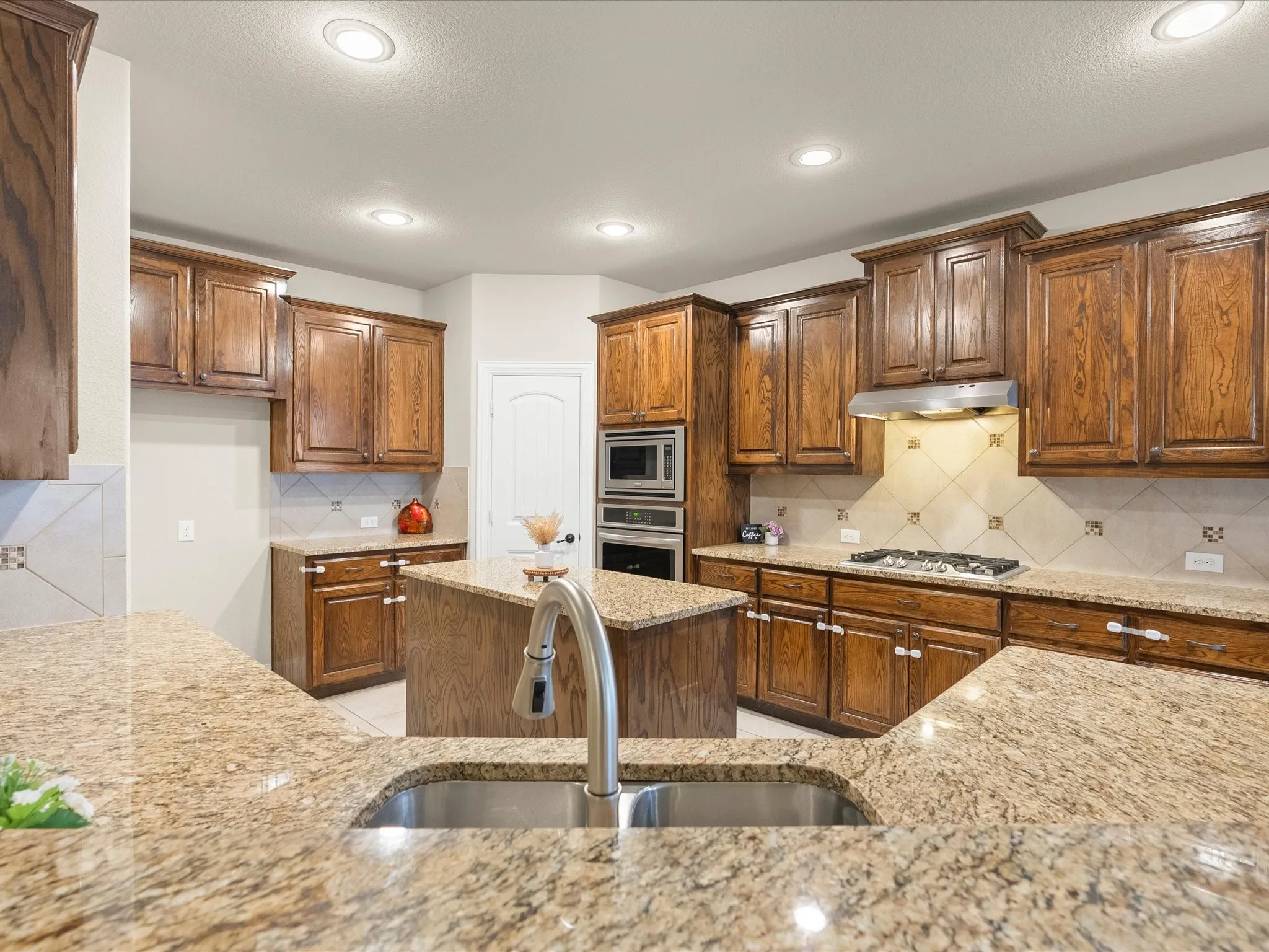 Kitchen featuring a central island, recessed lighting, built-in stainless steel appliances, a gas cooktop with an overhead vent, and extensive stone countertops