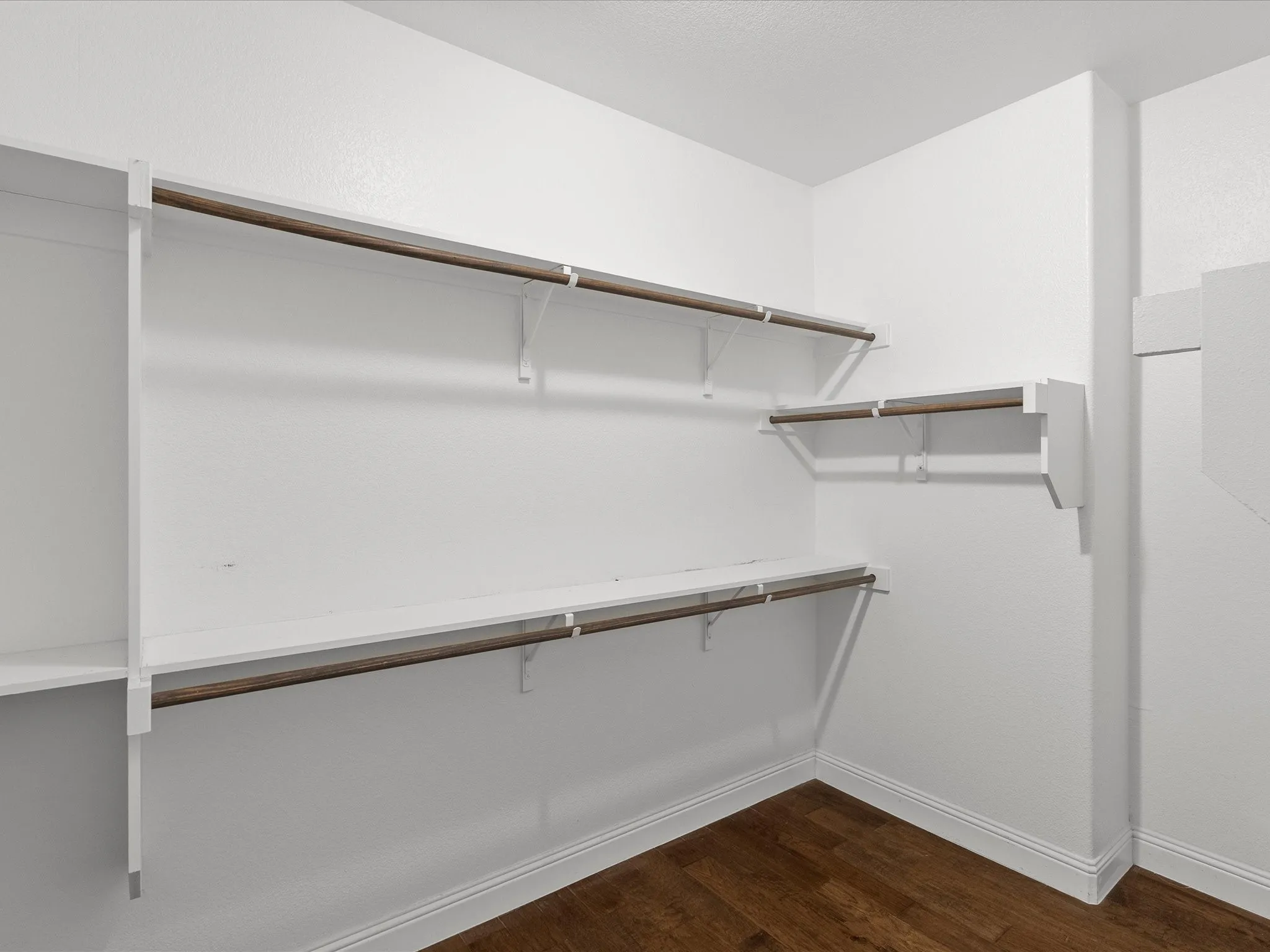 Walk-in closet with multiple hanging rods, shelving, and wood-finish flooring