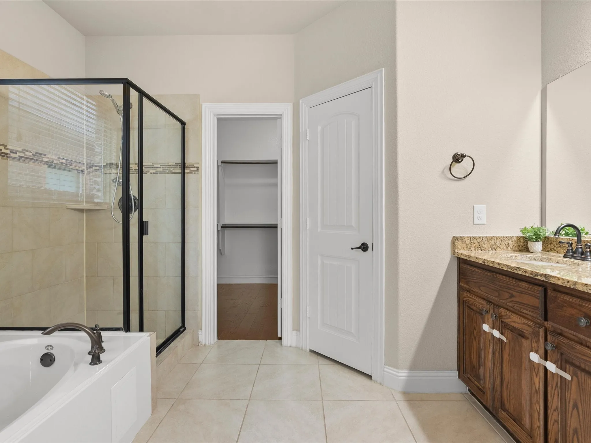 Spacious bathroom featuring a built-in bathtub, a walk-in shower with clear glass enclosure and tile surround, and a vanity with a granite countertop and wood-finish cabinetry