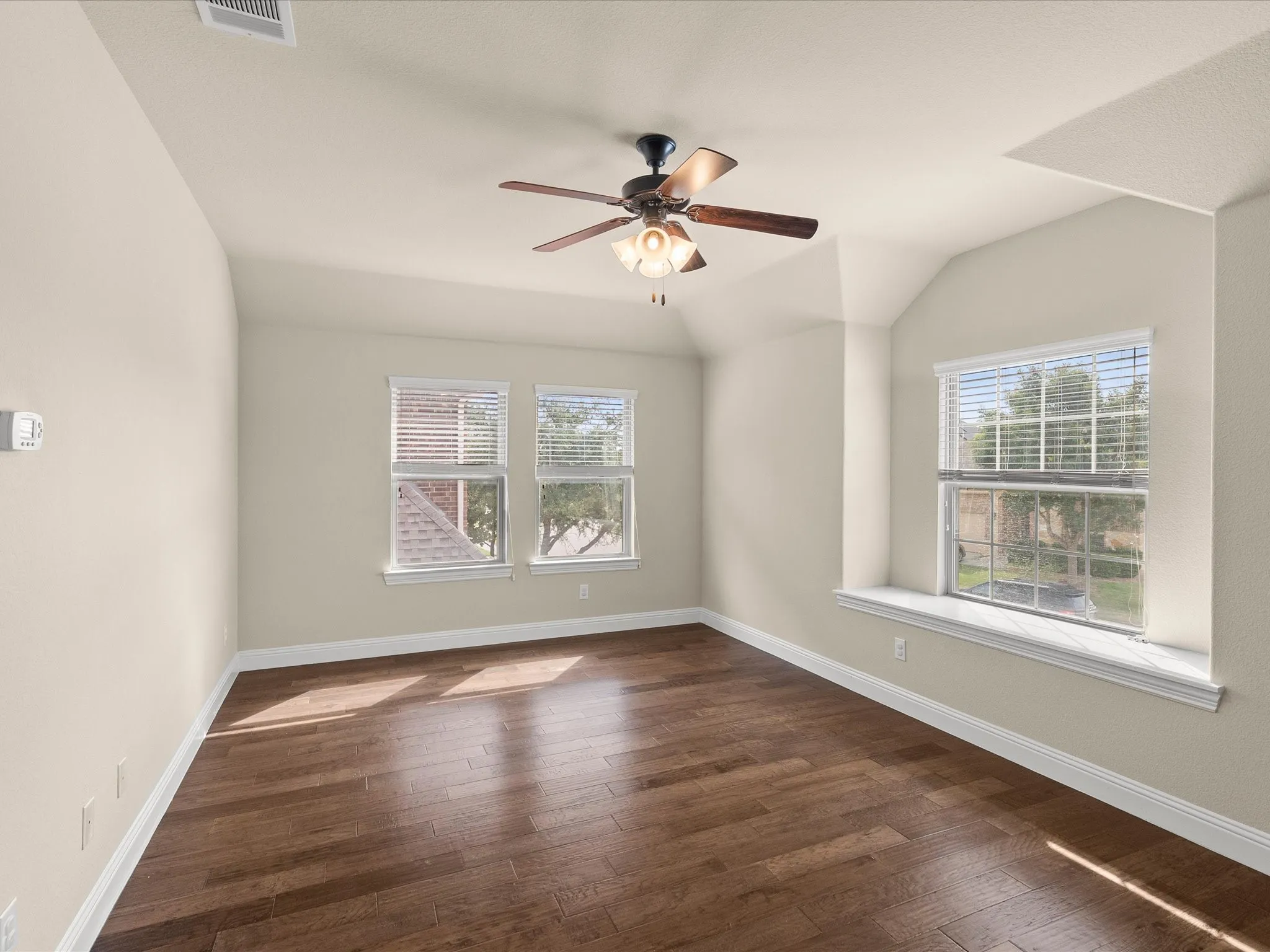 Wood-finish flooring, multiple windows with blinds, ceiling fan with light fixture, and vaulted ceiling