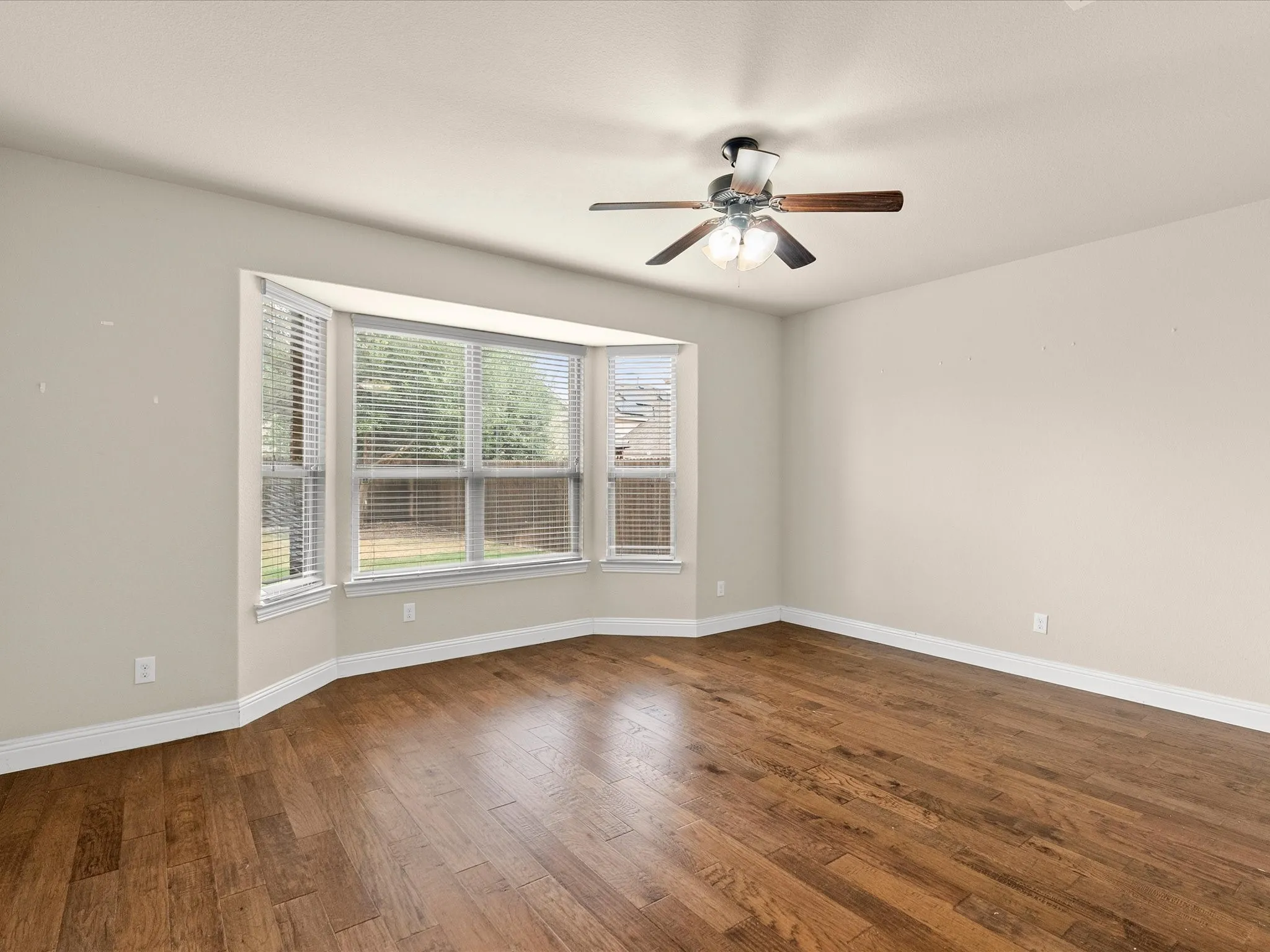 Bay window with blinds, wood-finish flooring, ceiling fan with light fixture, and neutral wall tones