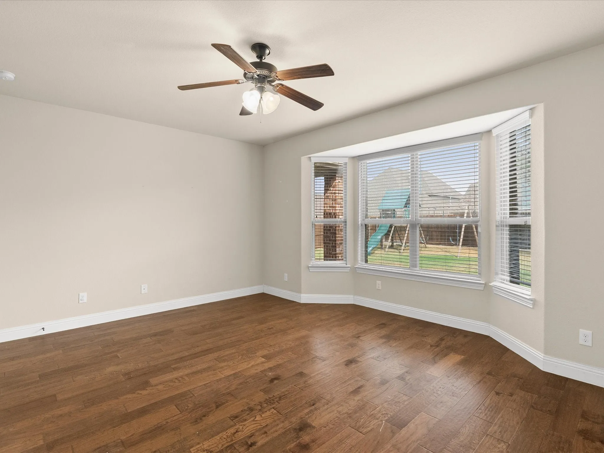 Wood-finish flooring, ceiling fan with integrated lighting, and multiple windows with blinds