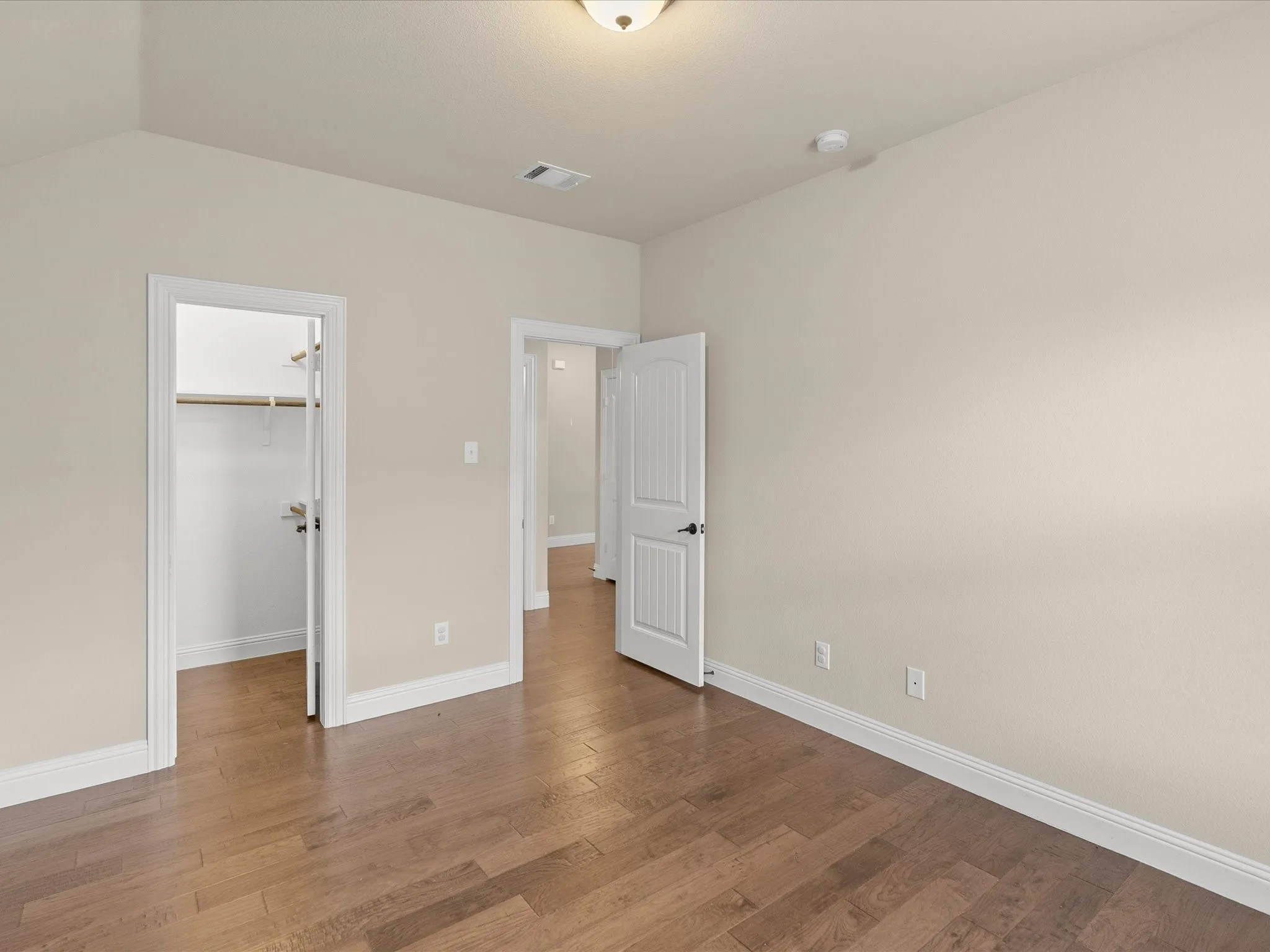 Wood-finish flooring, neutral wall paint, white trim, and a built-in closet with shelving