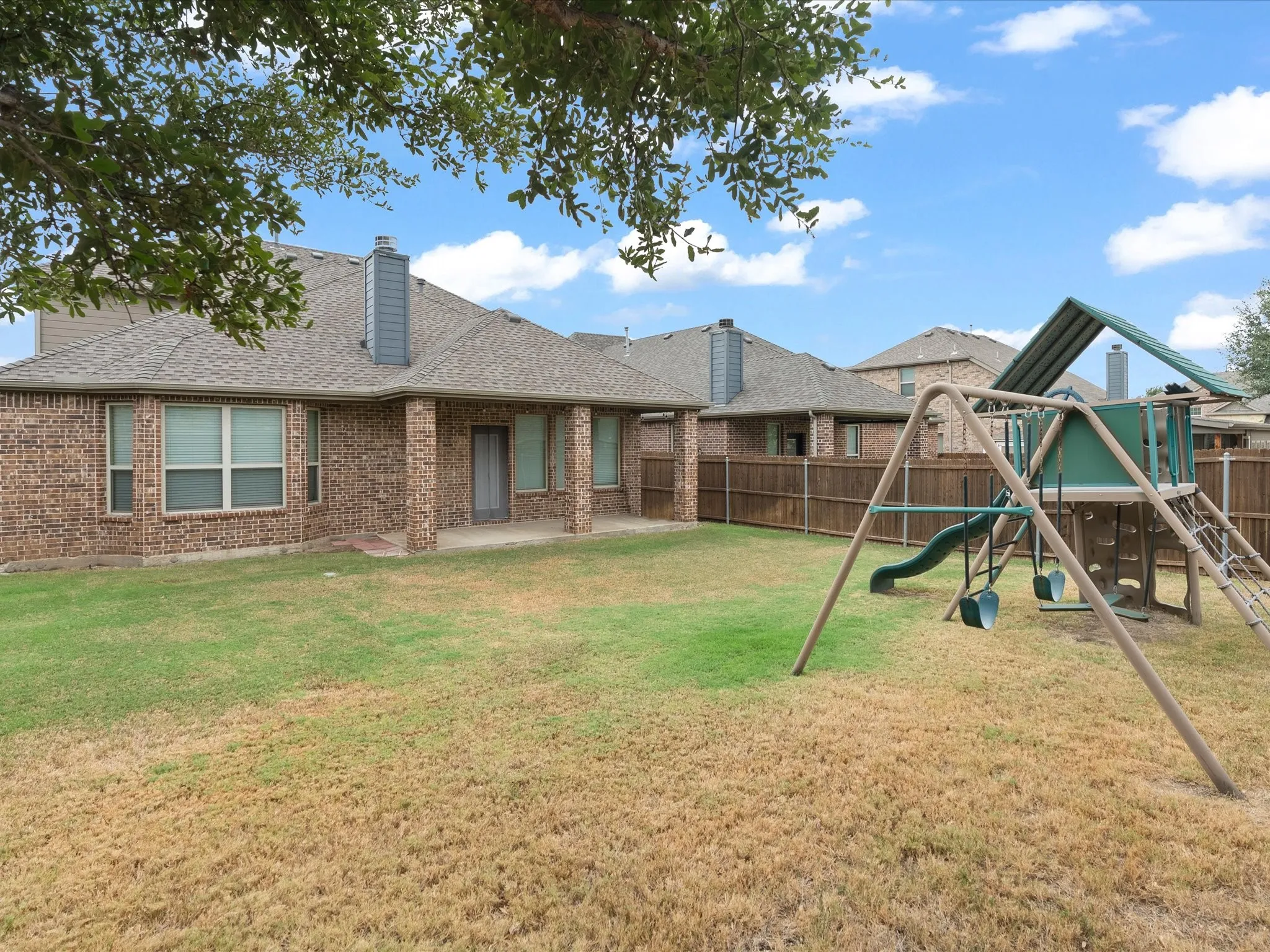 Expansive backyard with a covered patio, brick exterior, and a privacy fence