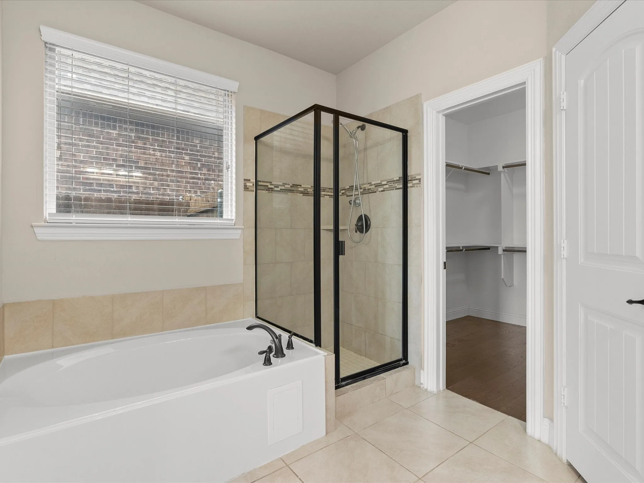 Built-in soaking tub with dark-toned fixtures, adjacent glass-enclosed shower with a tiled surround, and ceramic tile flooring