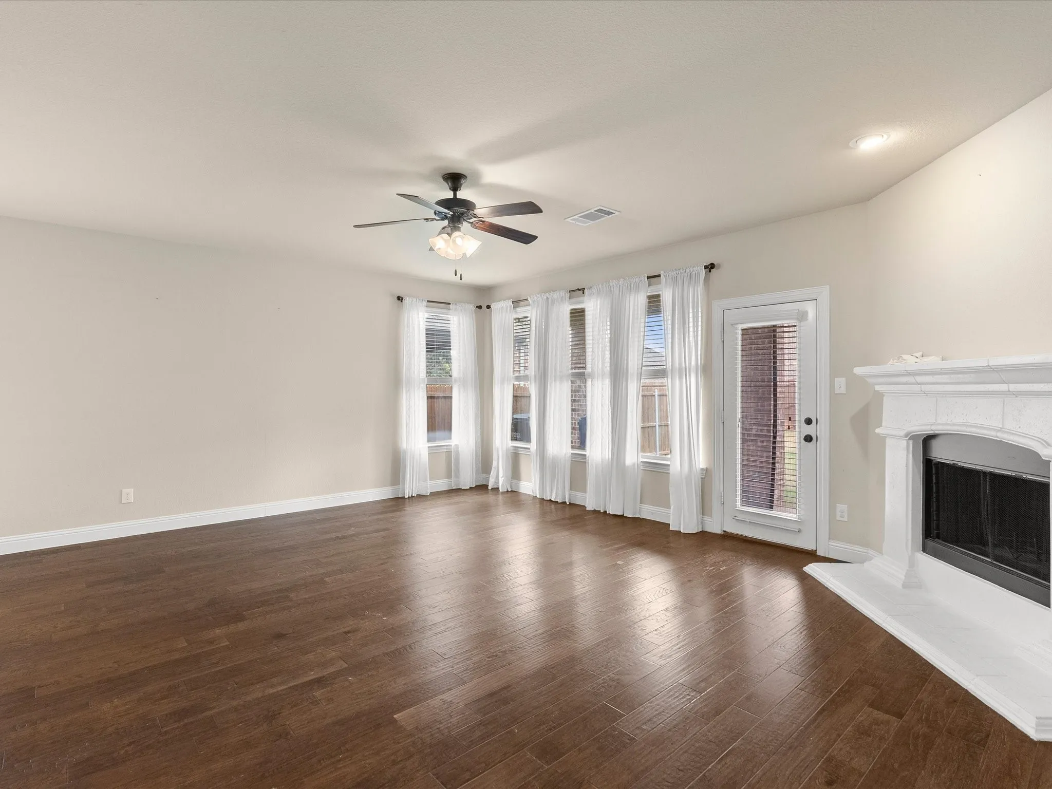 Wood-finish flooring, white fireplace with hearth, multiple windows, ceiling fan, and recessed lighting