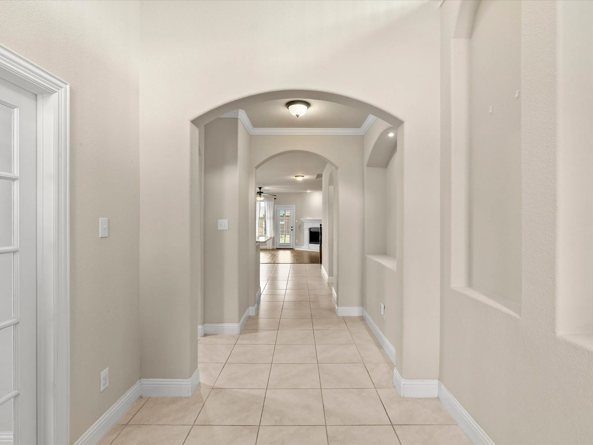 Arched doorways, recessed wall niches, crown molding, tile flooring, and a glass-paneled door