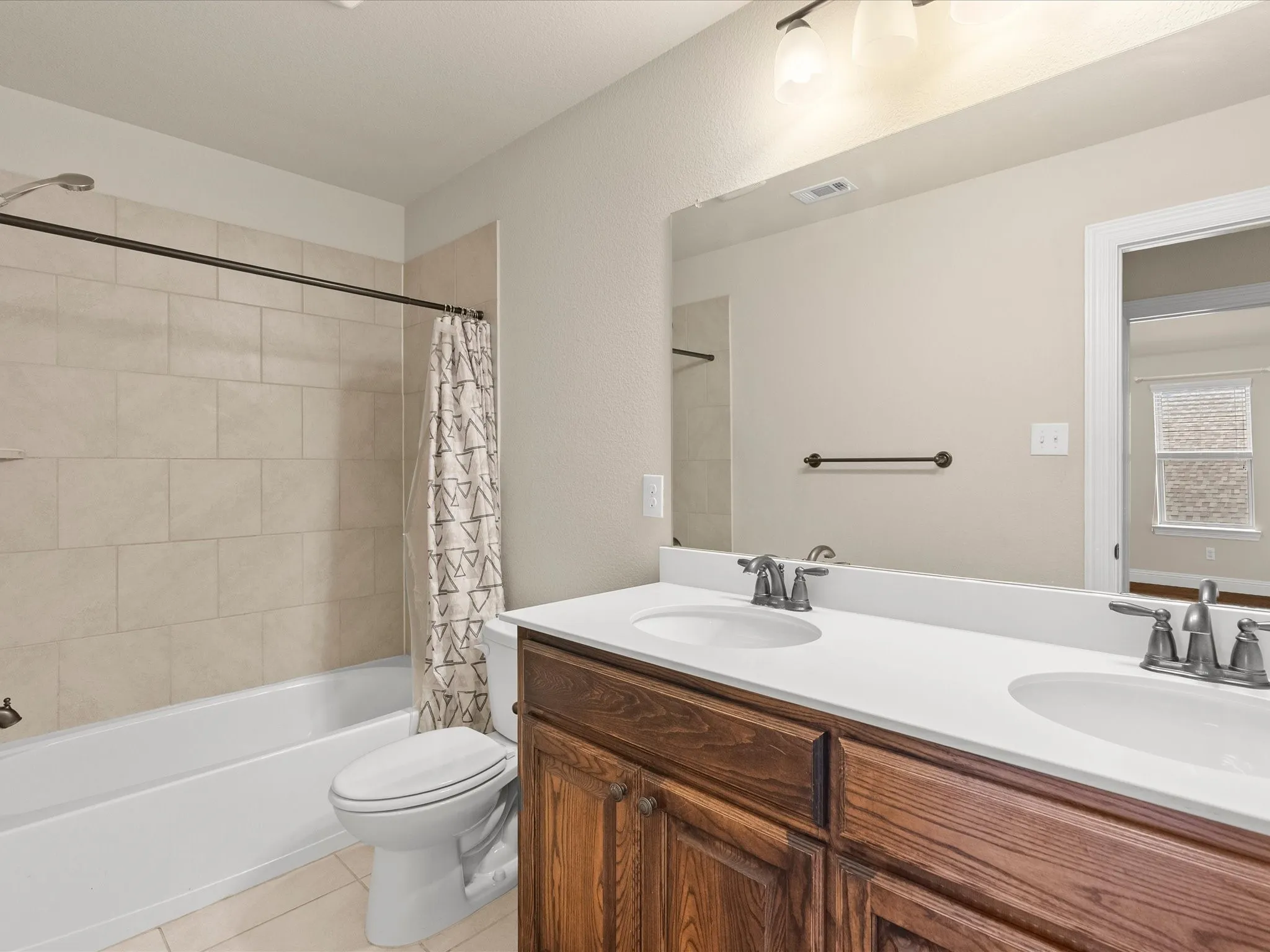 Bathroom featuring a dual-sink vanity with a white countertop, wood-finish cabinetry, and a bathtub with tiled surround